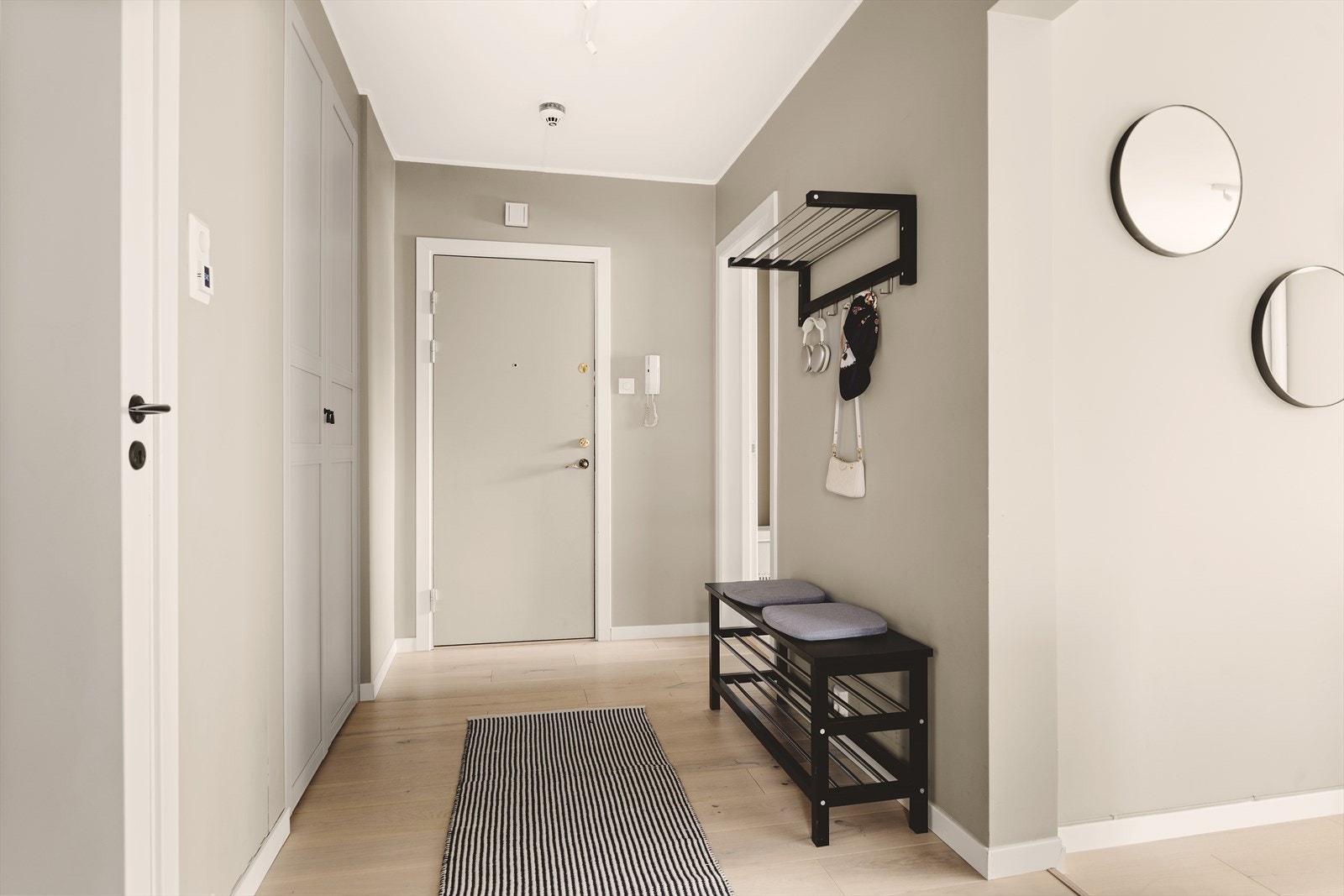 Innbydende entré med god plass til henging av yttertøy, skoskap eller annen oppbevaring. Porttelefon på vegg, dørklokken inn til bygget er appstyrt og kan åpnes direkte fra telefonen Galleribilde