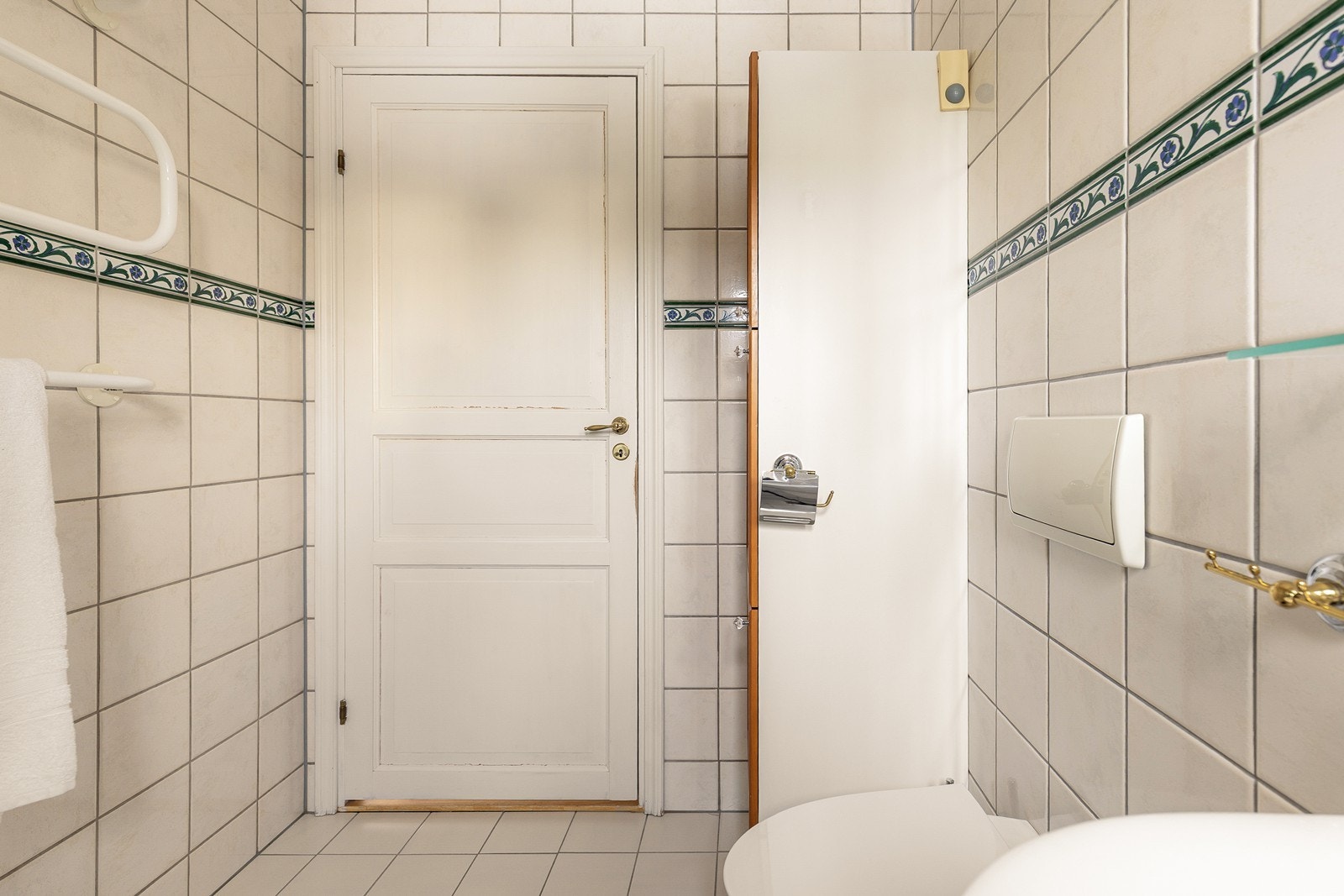 Badet har hvite 20x20 cm fliser på gulv og vegger, med en dekorativ bord. Galleribilde
