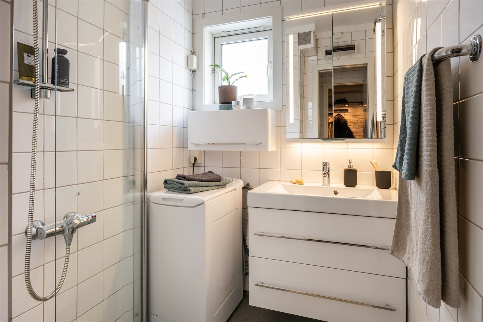 Badet er utstyrt med innfellbare dusjvegger av glass, gulvmontert toalett, innredning med servant og vaskemaskin som medfølger handelen. Galleribilde