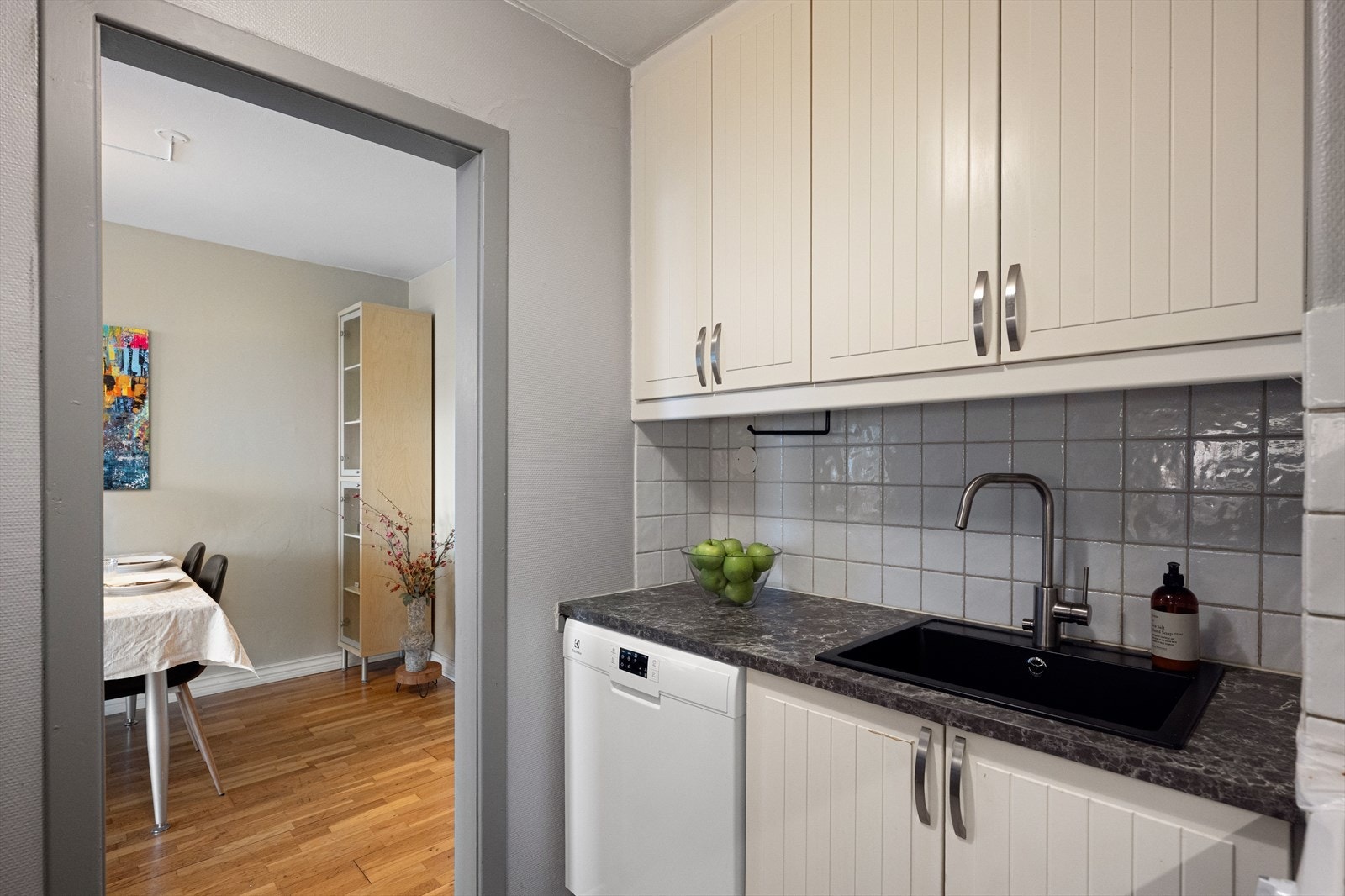 Kjøkkenet er innredet med over og underskap og fliser over kjøkkenbenken. Galleribilde