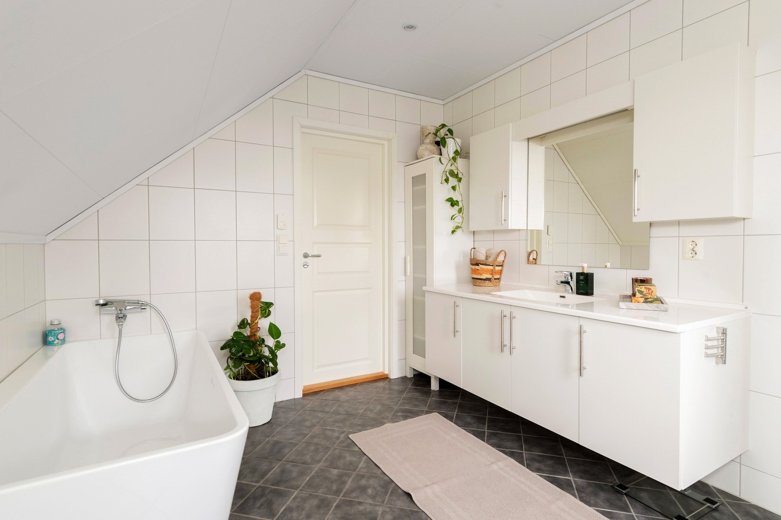 Badet er utsyrt med baderomsinnredning, heldekkende servantplate, badekar, vegghengt wc, speil og veggskap. Galleribilde