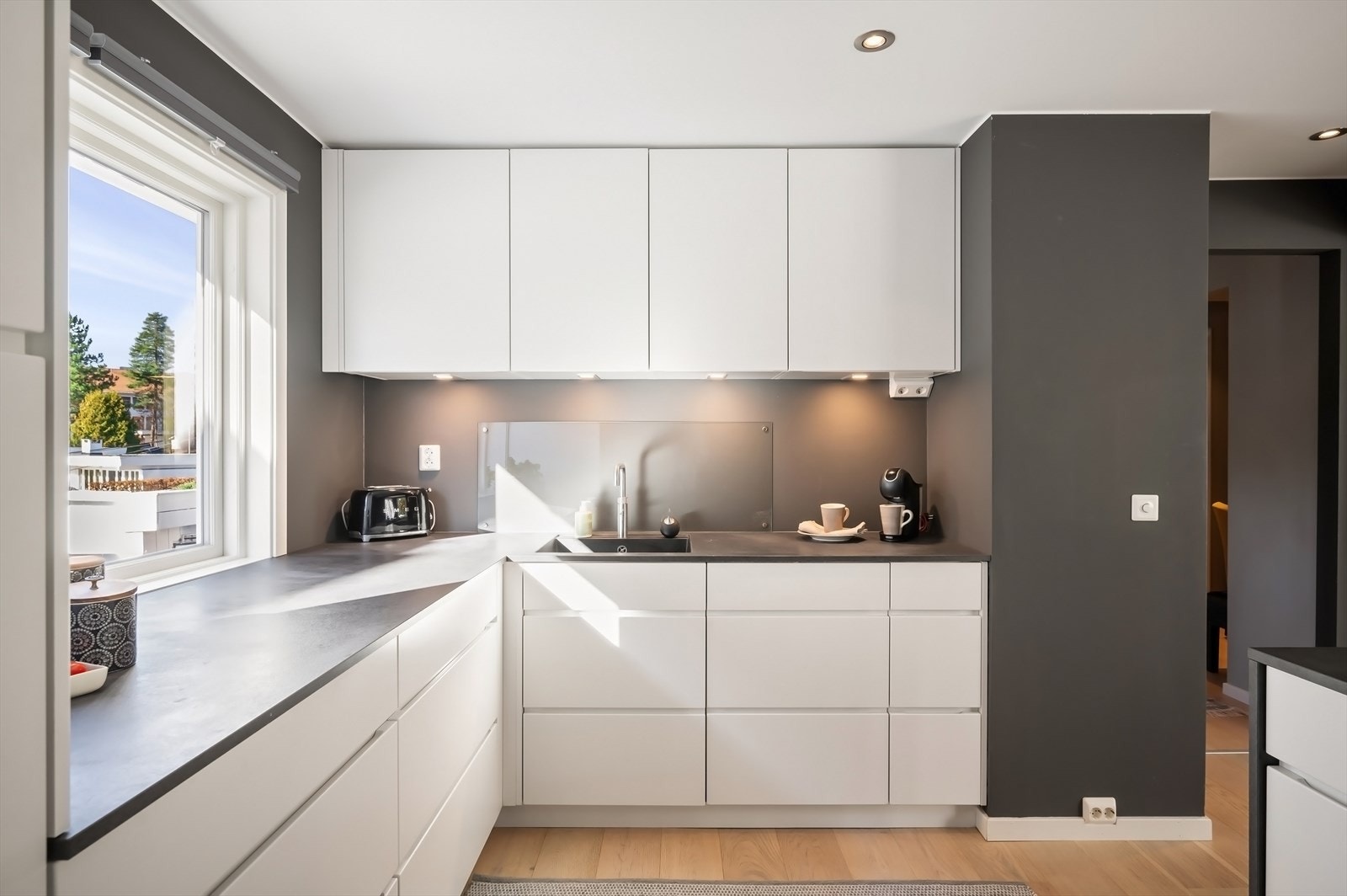 Innredning med slette fronter, nedfelt oppvaskkum i benk, downlights under overskap og integrerte hvitevarer. Galleribilde