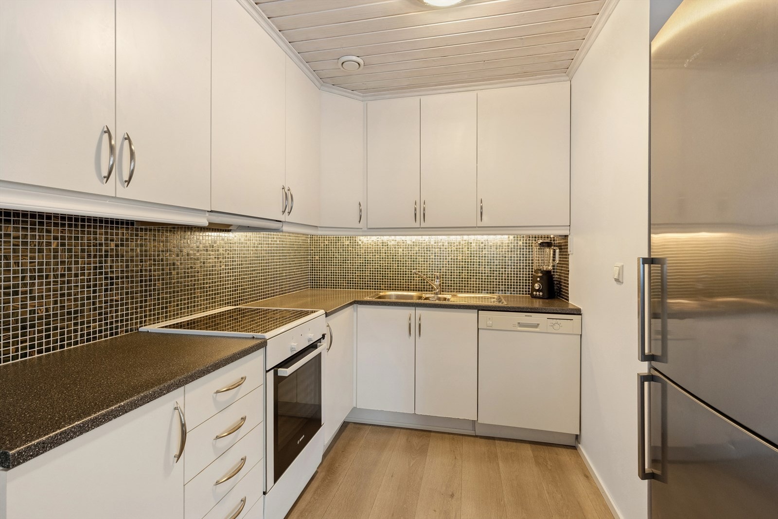 Kjøkkenet har hvite glatte fronter, benkeplate av laminat og frittstående hvitevarer. Galleribilde