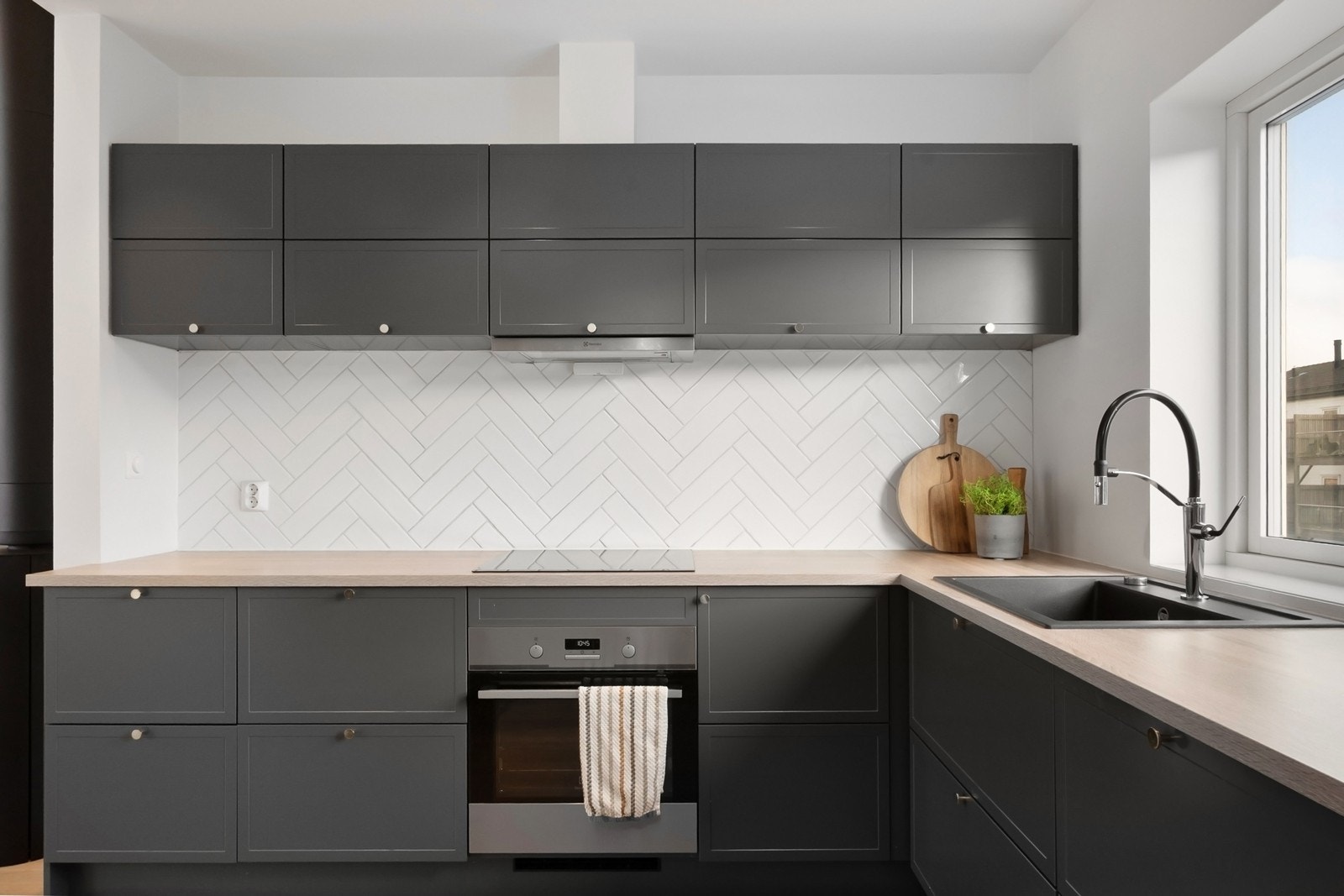 Over benk er det hvite fliser i fiskebensmønster på vegg, kjøkkenventilator med avtrekk ut og det er installert automatisk vannstoppventil. Galleribilde