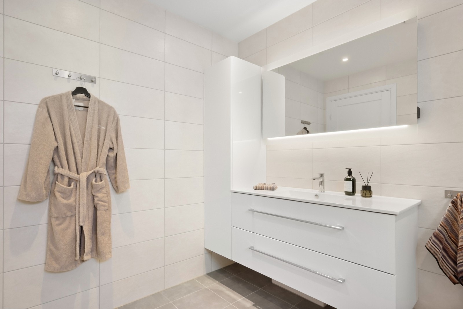 Badet har skuffer og skap for oppbevaring, stort speil med lys og dusjnisje med glassvegger, regnfallsdusj og mosaikkflis. Galleribilde