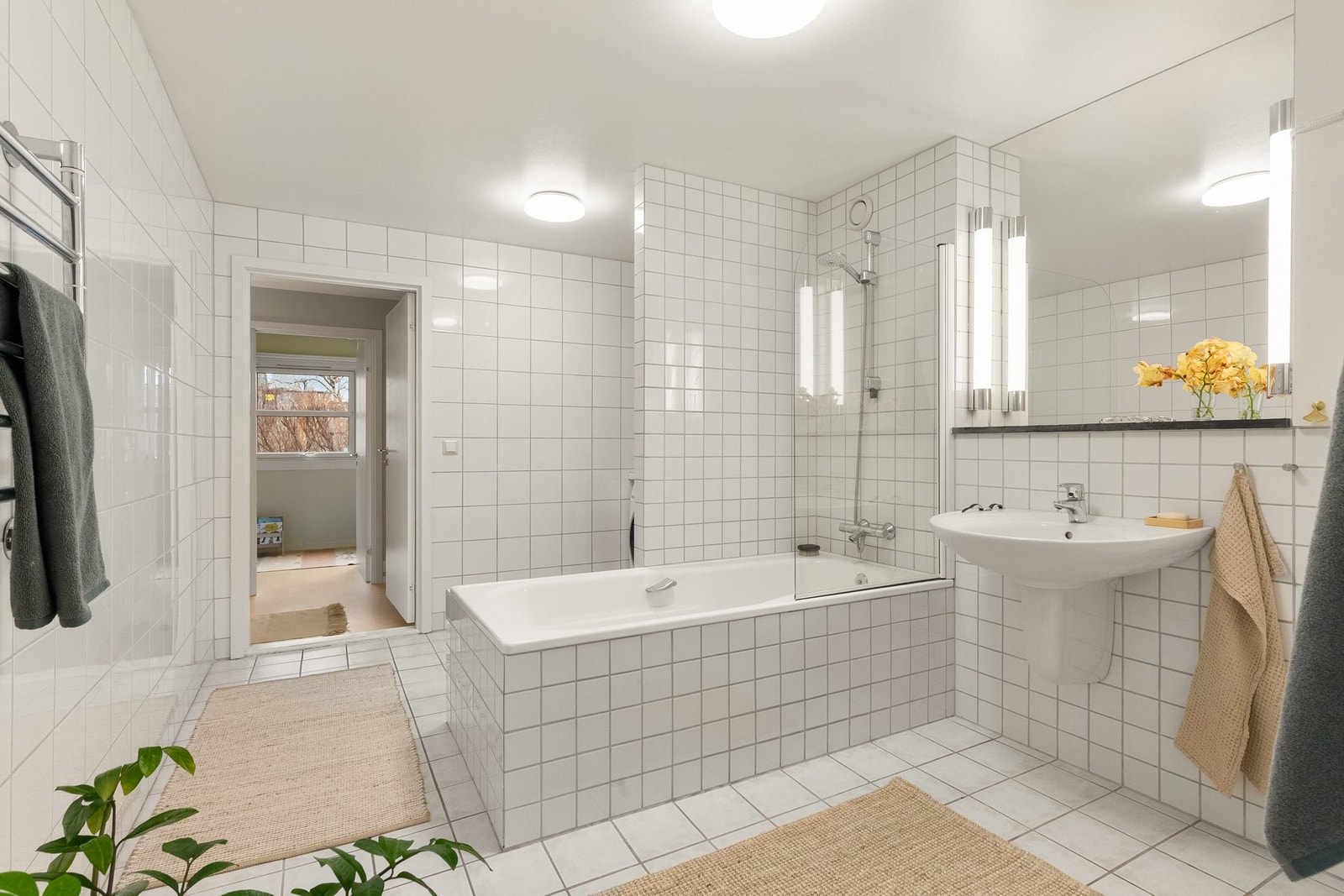 Videre inneholder baderommet servant på vegg, speil med lysarmatur over servant, veggmontert håndkletørker, veggmontert klosett, innfliset badekar med halvvegg i glass og termometerstyrt blandebatteri. Galleribilde