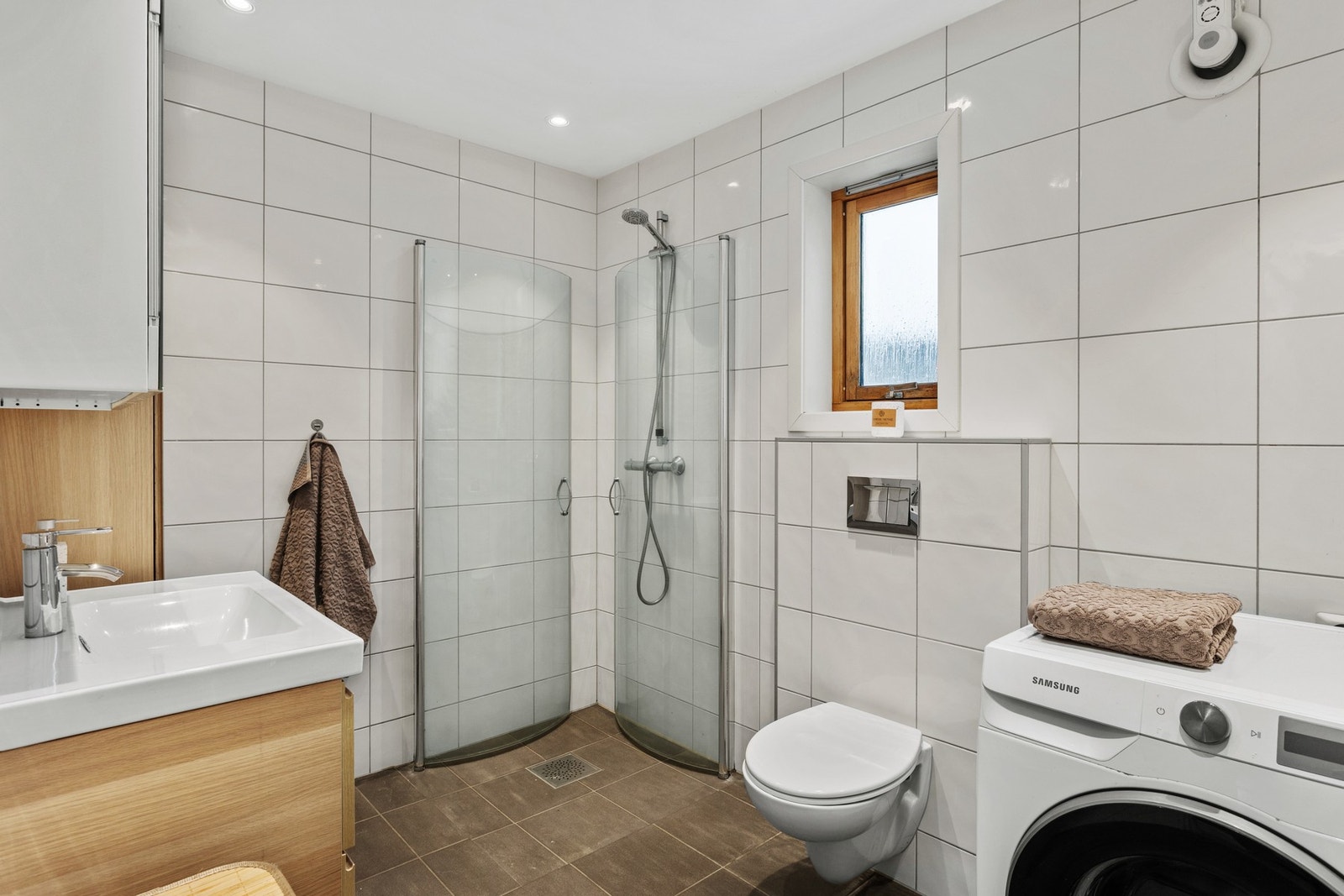 Badet er innredet med vegghengt toalett, servantinnredning, speilskap og dusjhjørne med innfellbare glassdører. Videre er det opplegg for vaskemaskin Galleribilde