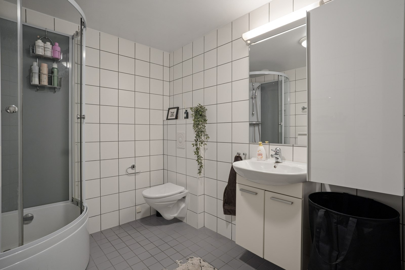 Badet er helfliset og utstyrt med veggmontert toalett, servantinnredning og dusjkabinett. Galleribilde