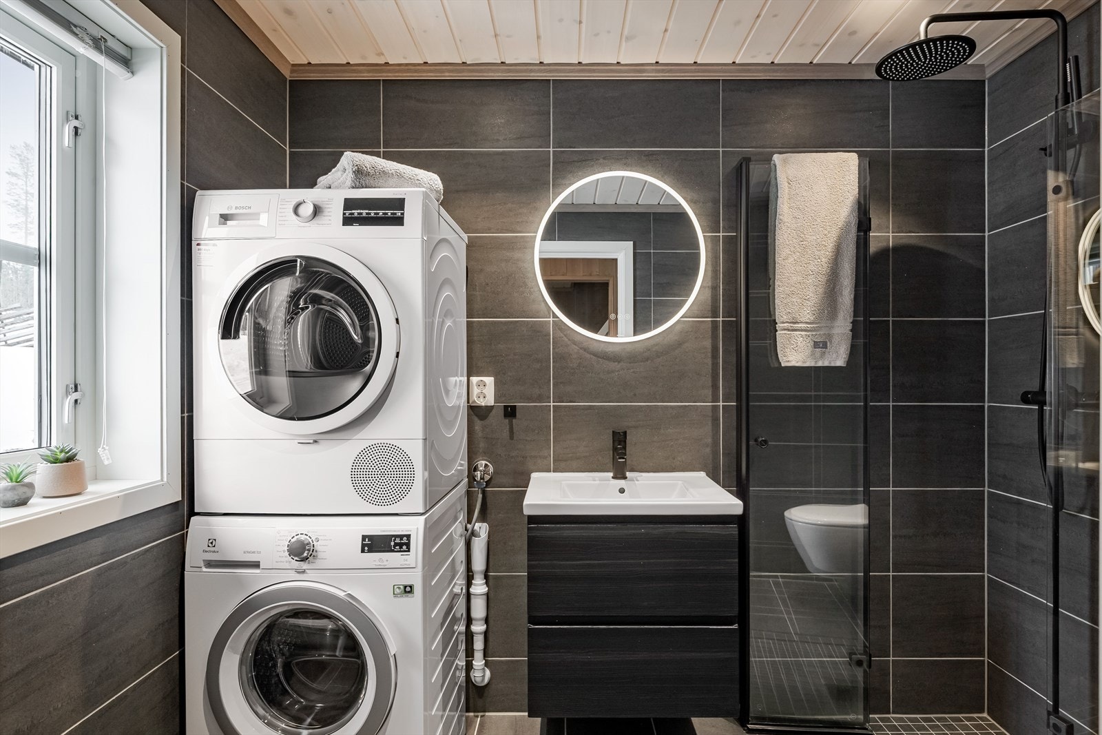 Hyttas hovedbad med adkomst fra gangen er innredet med servant på innredning, toalett, dusjhjørne med glassvegger og opplegg for vaskemaskin/tørketrommel. Det er også her varmekabler i gulvet. Galleribilde