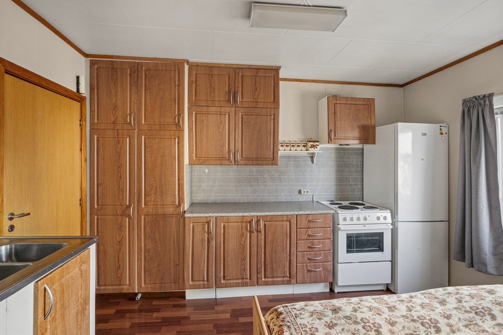 Kjøkkenet har eldre innredning med mørke profilerte fronter og laminert benkeplate med beslagvask. Galleribilde