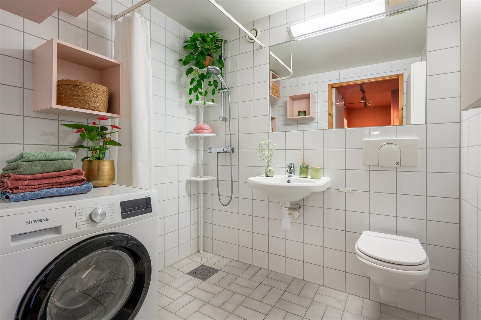 Lyst flislagt og tidløst bad med varmekabler i gulv. Badet er innredet med servant, toalett, dusjhjørne og opplegg for vaskemaskin. Galleribilde