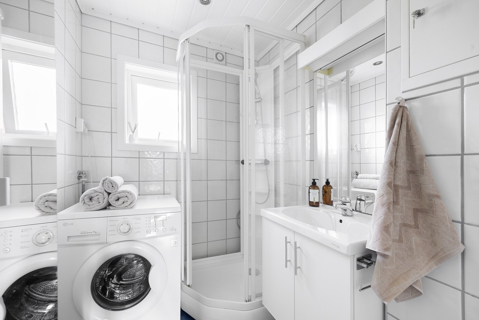 Badet er innredet med servant i innredning, vegghengt toalett, dusjkabinett og opplegg for vaskemaskin. Galleribilde