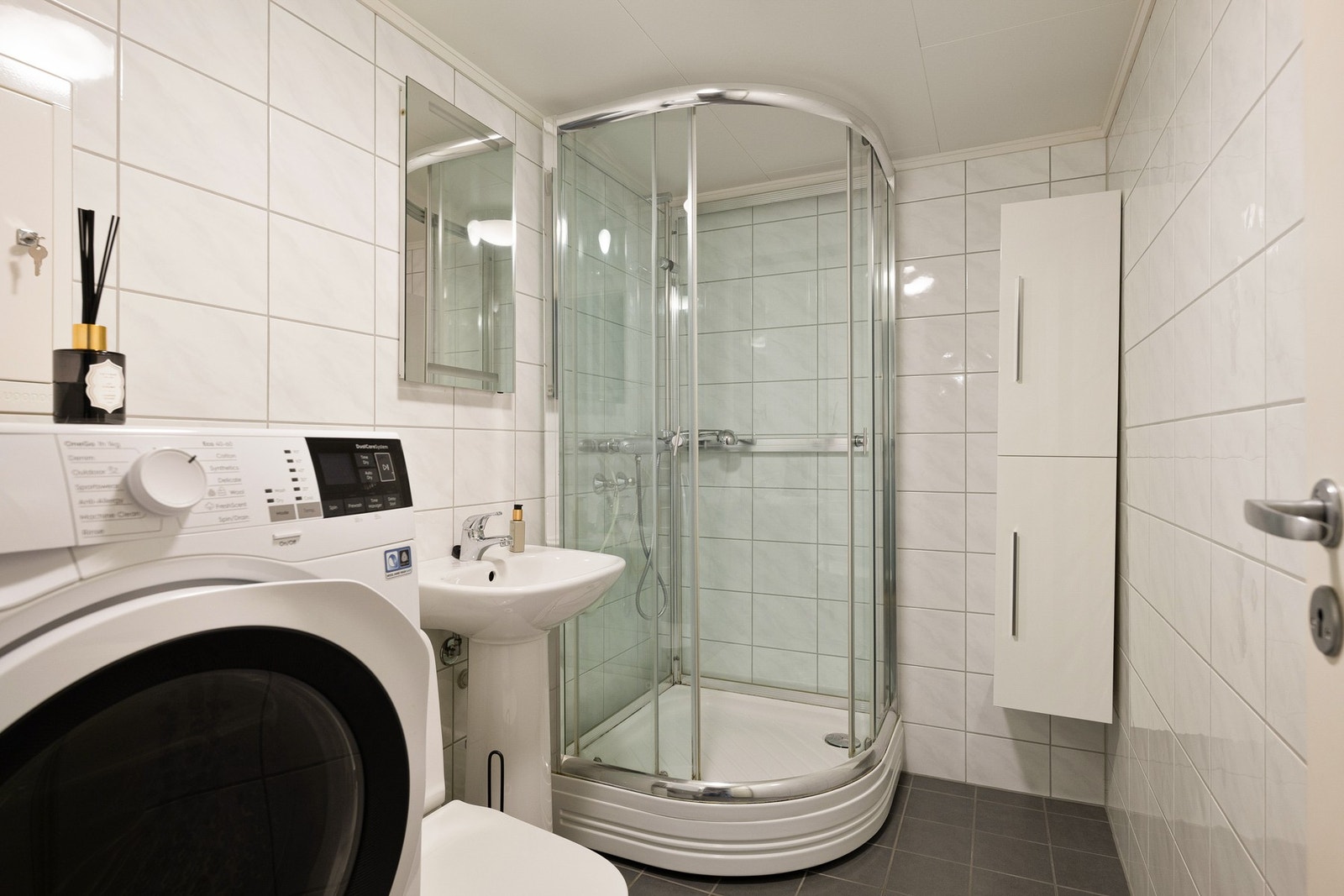 Pent og flislagt bad med varmekabler i gulvet. Badet inneholder wc, servant, dusjkabinett, høyskap med slette høyglans fronter og opplegg for vaskemaskin. Galleribilde