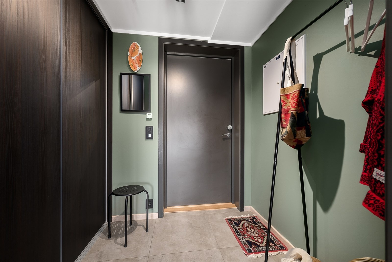 Gangen har plass til garderobeskap og til å henge fra seg yttertøy og utstyr. Veggene er malt i en trendy grønntone. Fliser på gulv. Galleribilde