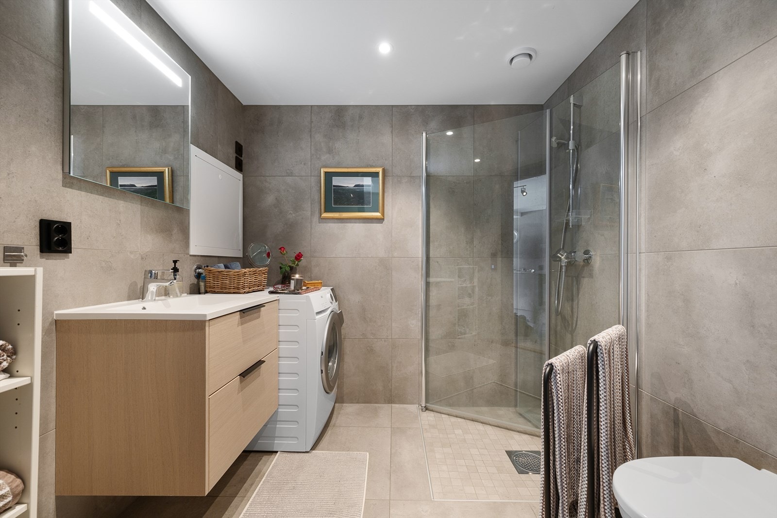 Delikat, tidløst og innbydende bad med dusjhjørne, wc, servantinnredning og opplegg for vaskemaskin. Galleribilde