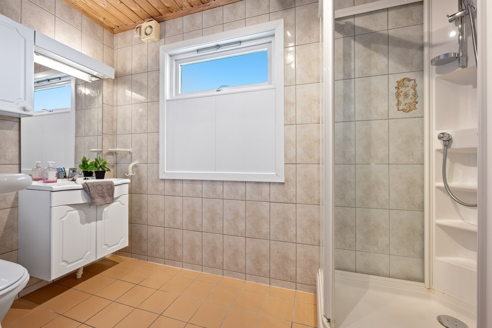 Flislagt bad med dusjkabinett, servant i innredningen og toalett. Galleribilde