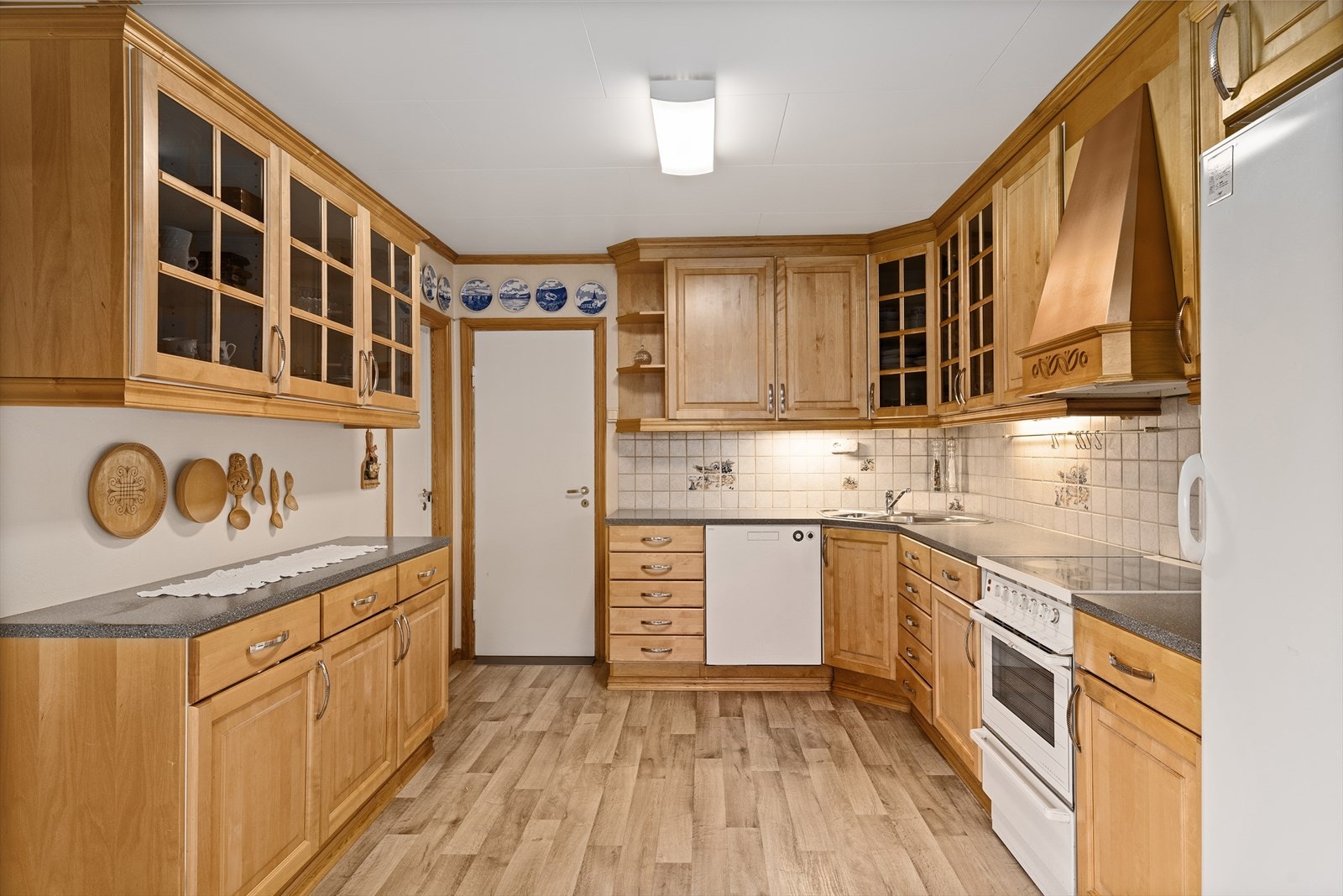 Profilert kjøkkeninnredning med laminat benkeplate og fliser over benk. Overskap til tak. Galleribilde