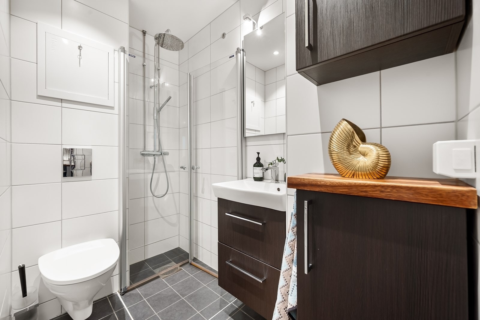 Badet er innredet med vegghengt toalett, dusjhjørne med svingbare glassdører og servant nedfelt i innredning. Galleribilde