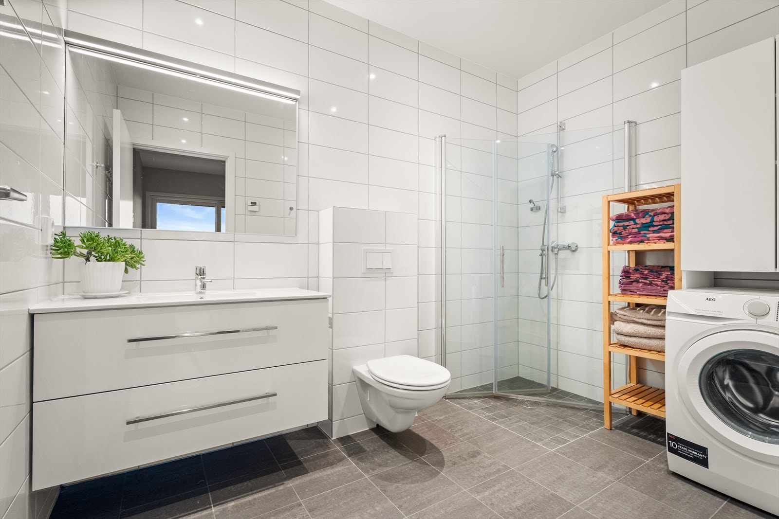 Leilighetens hovedbad er flislagt og utstyrt med dusjhjørne og opplegg for vaskemaskin. Galleribilde