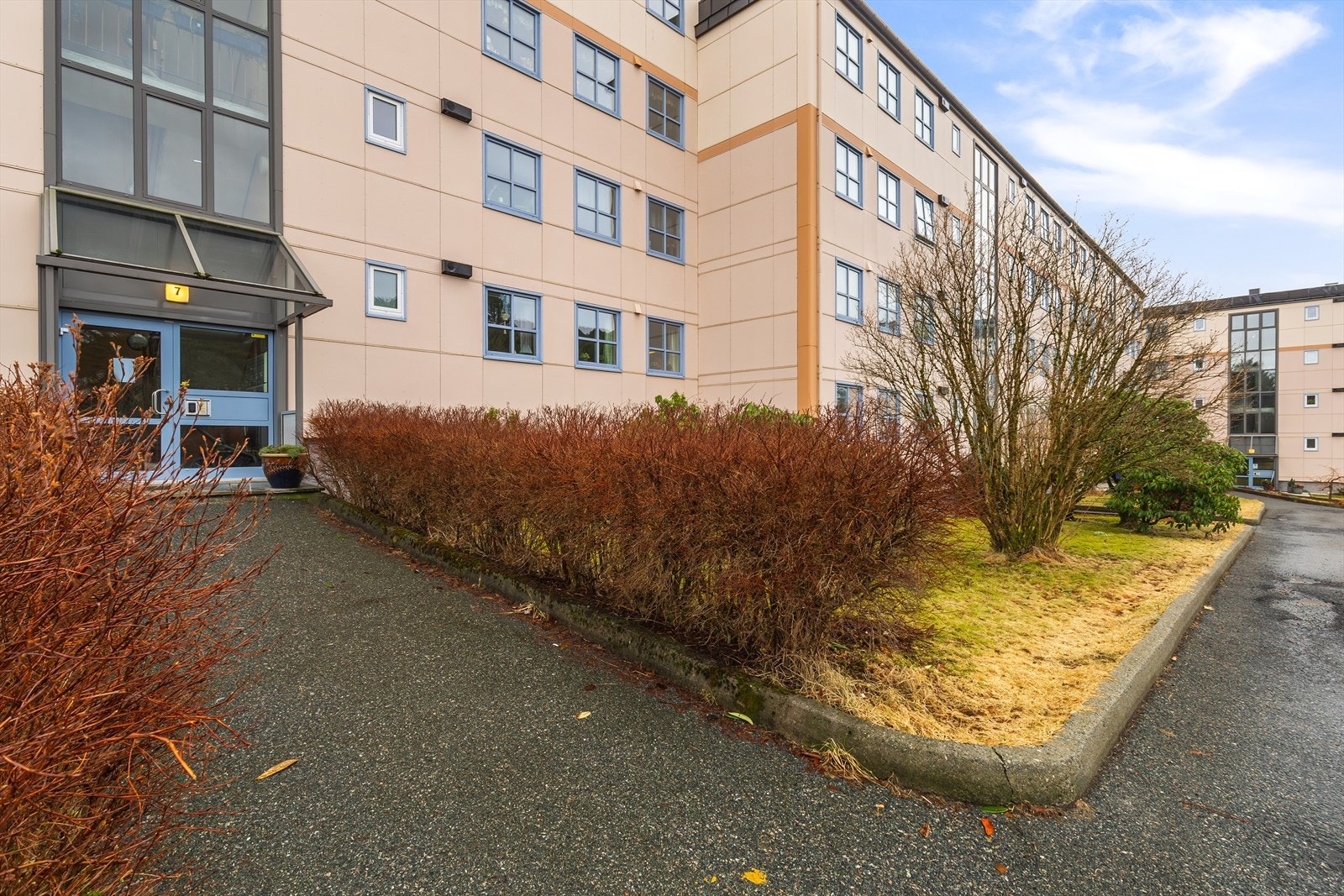 Adkomsten til bygningen er via en asfaltert gangvei, omkranset av busker og grøntarealer. Galleribilde