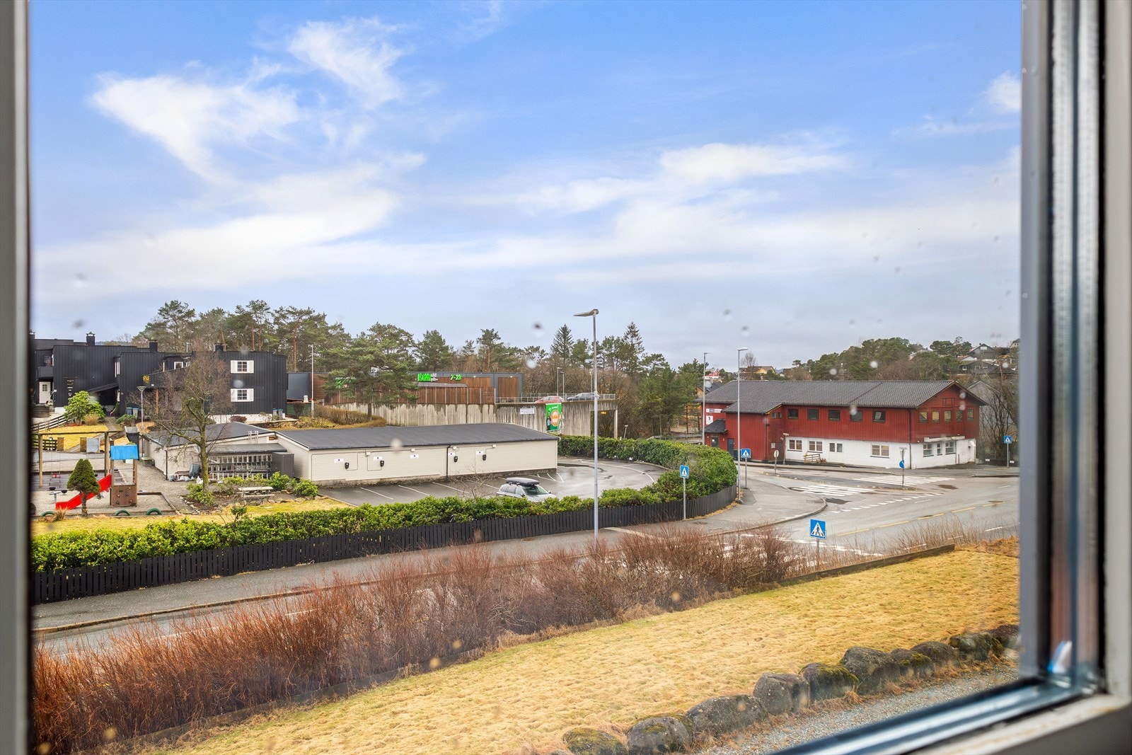 Utsyn mot nærliggende butikk og grøntarealer fra vinduet. Galleribilde