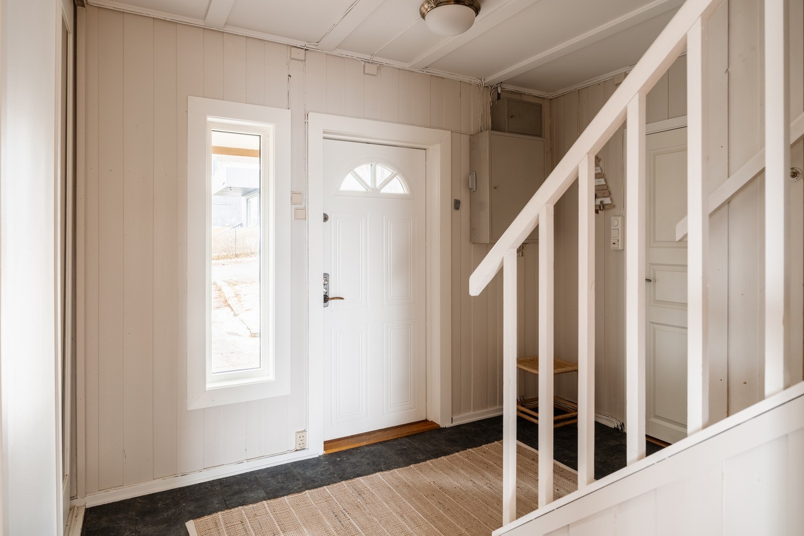 Velkommen inn i boligens entré. Her er gulvet belagt med laminatfliser, mens veggene har malt panel som bidrar til et klassisk uttrykk. Galleribilde