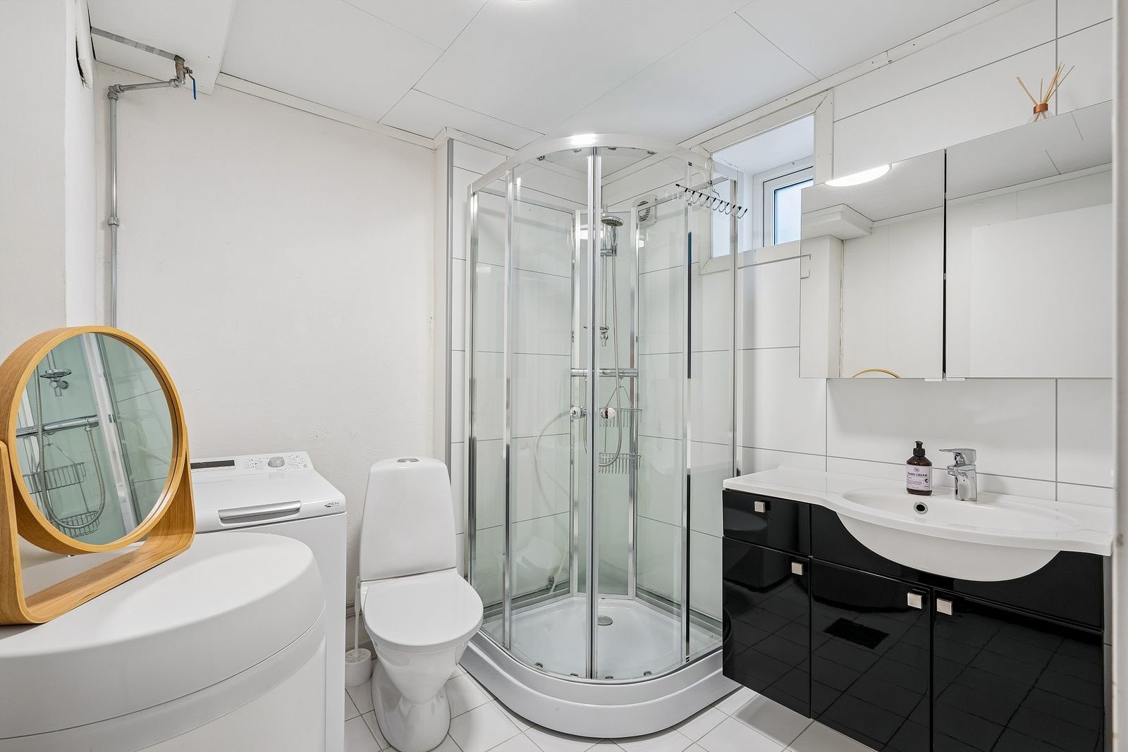 Baderom med flislagt gulv, dusjkabinett og vaskemaskin.