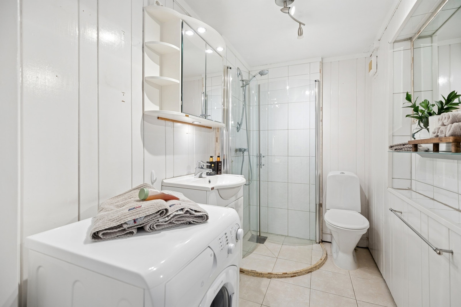 Hybel: Badet har fliser på gulv med gulvvarme. Dusjhjørne med innfellbare dører, lys servantinnredning, gulvstående toalett og opplegg for vaskemaskin. Galleribilde