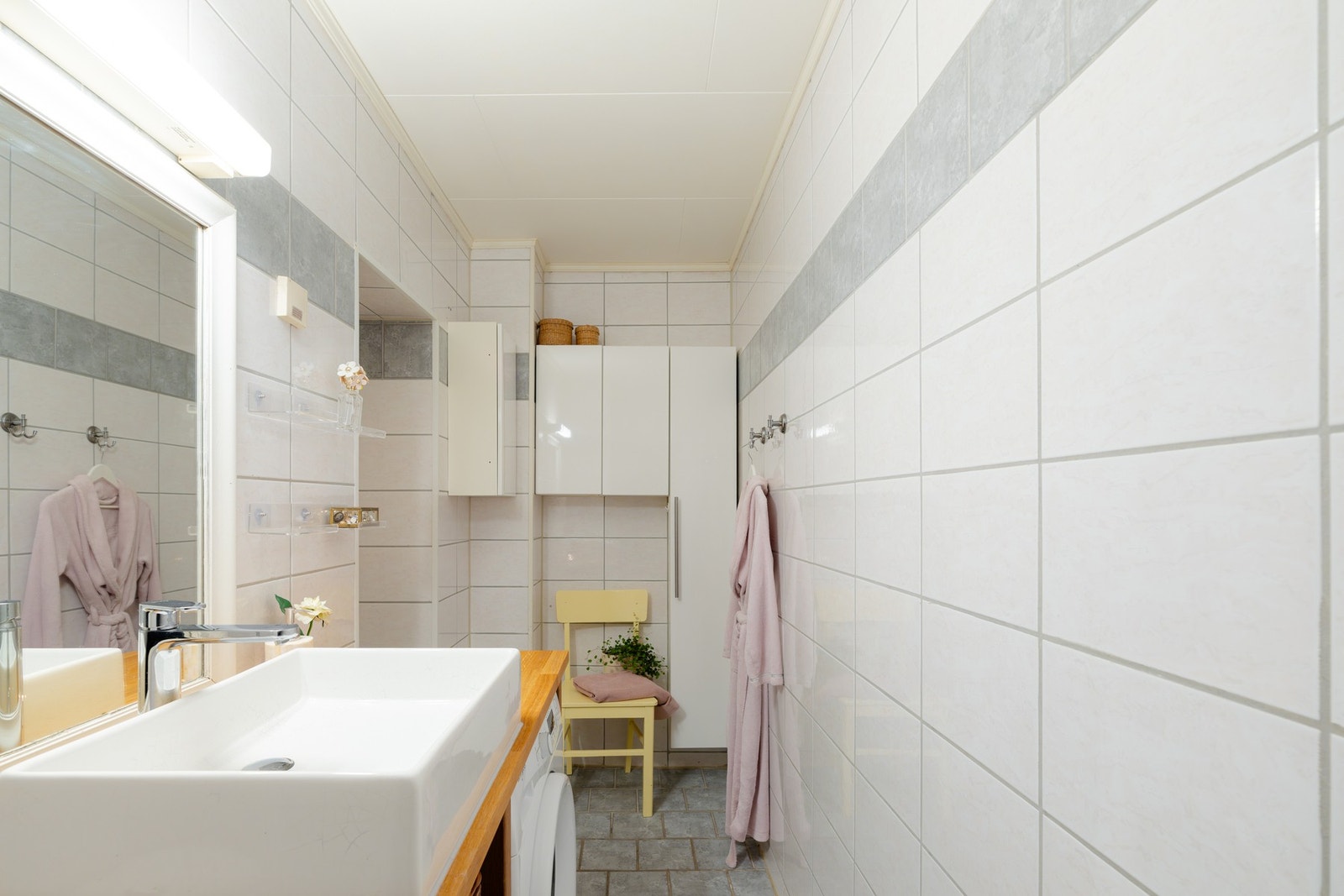 Videre er det ovenpåliggende servant med hyller på underside, speil med overbelysning og vegghengte skap. Galleribilde