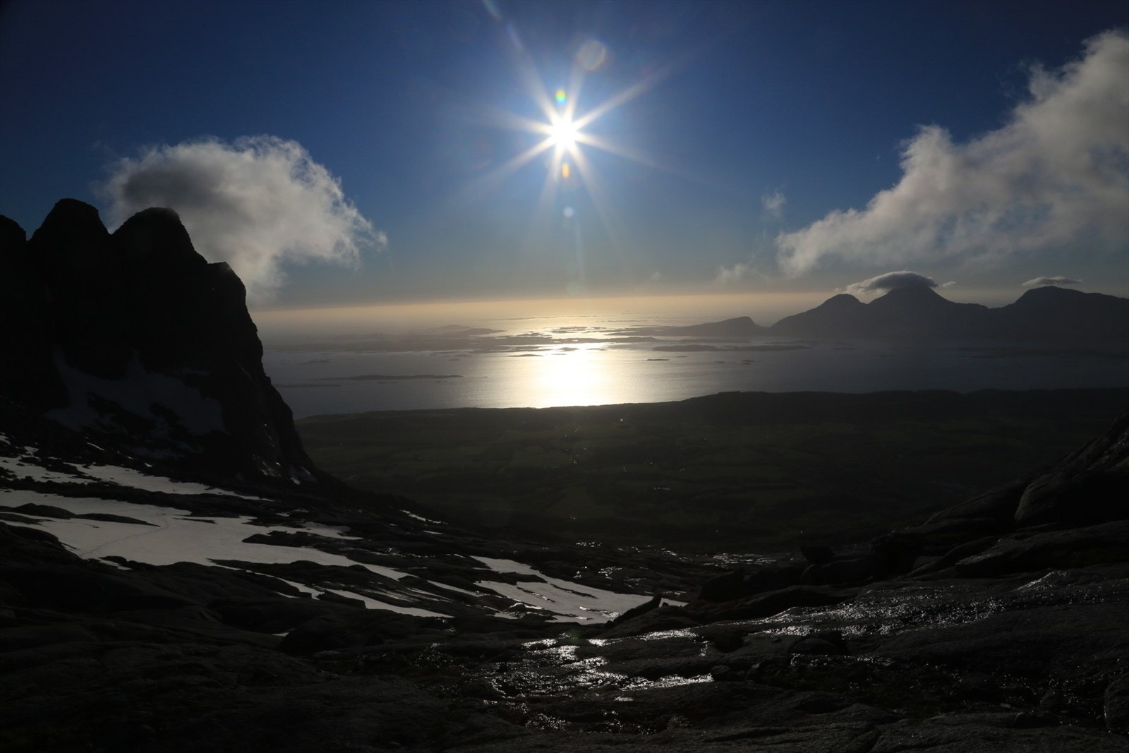 Utsikt fra De syv søstre og vestover, vi ser Dønnamannen og t.v. for Dønnamannen øyriket i Herøy. Seløya ligger rett under solen på bildet. Galleribilde