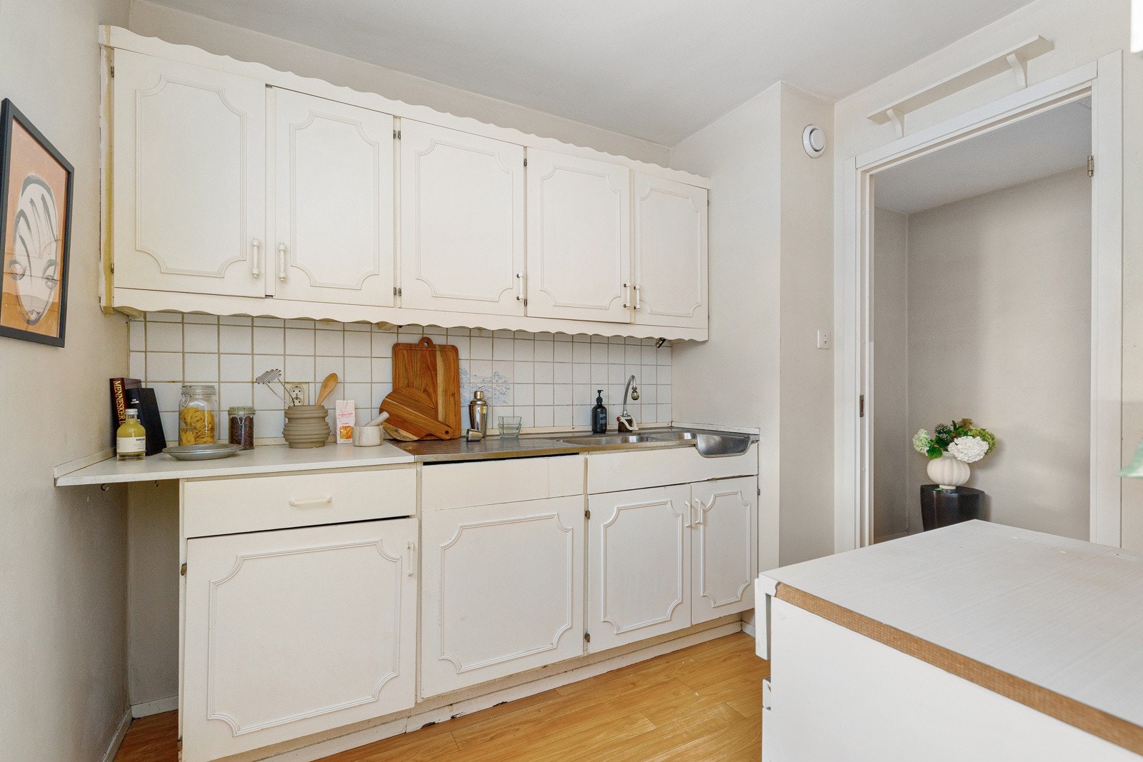 Eldre kjøkken med profilerte fronter, laminert benkeplate og benkeplate i rustfritt stål med formstøpt oppvaskkum med svingbart blandebatteri. Galleribilde