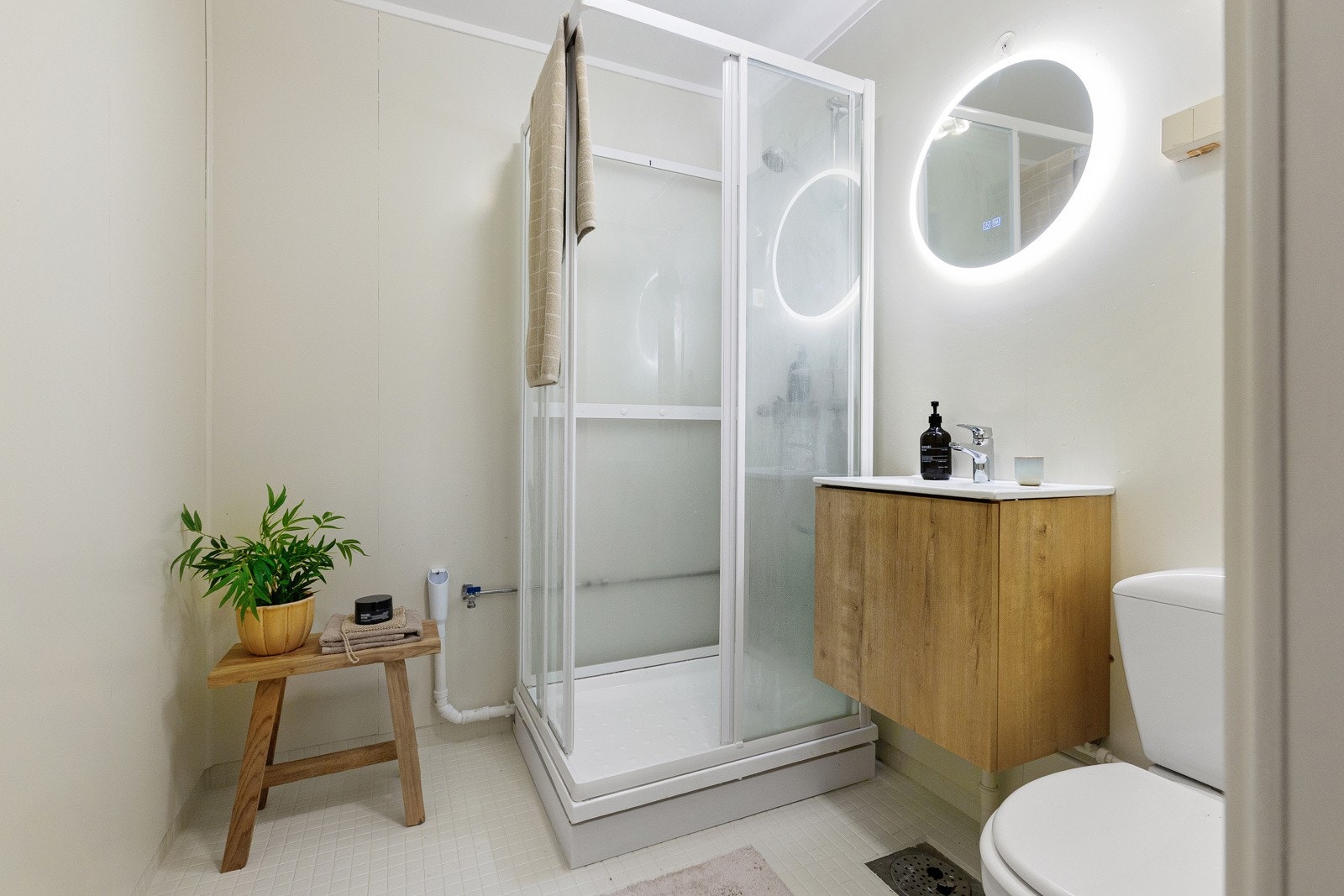 Badet er utstyrt med dusjkabinett, gulvmontert toalett, hvit servant med blandebatteri. Galleribilde