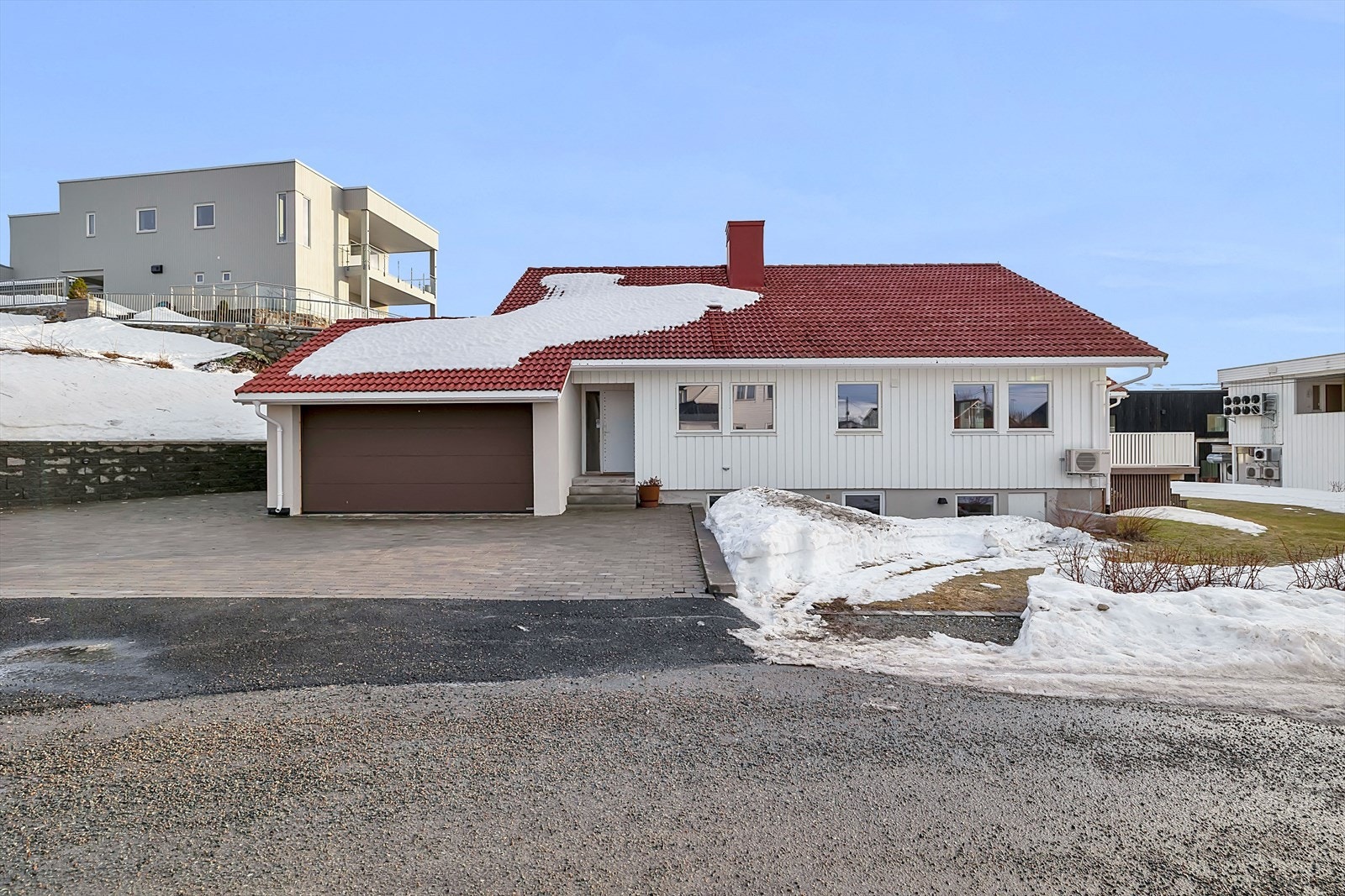 Steinbelagt og dels asfaltert adkomst. Støttemur bygget opp for god plass rundt det østlige hjørnet av huset. Galleribilde