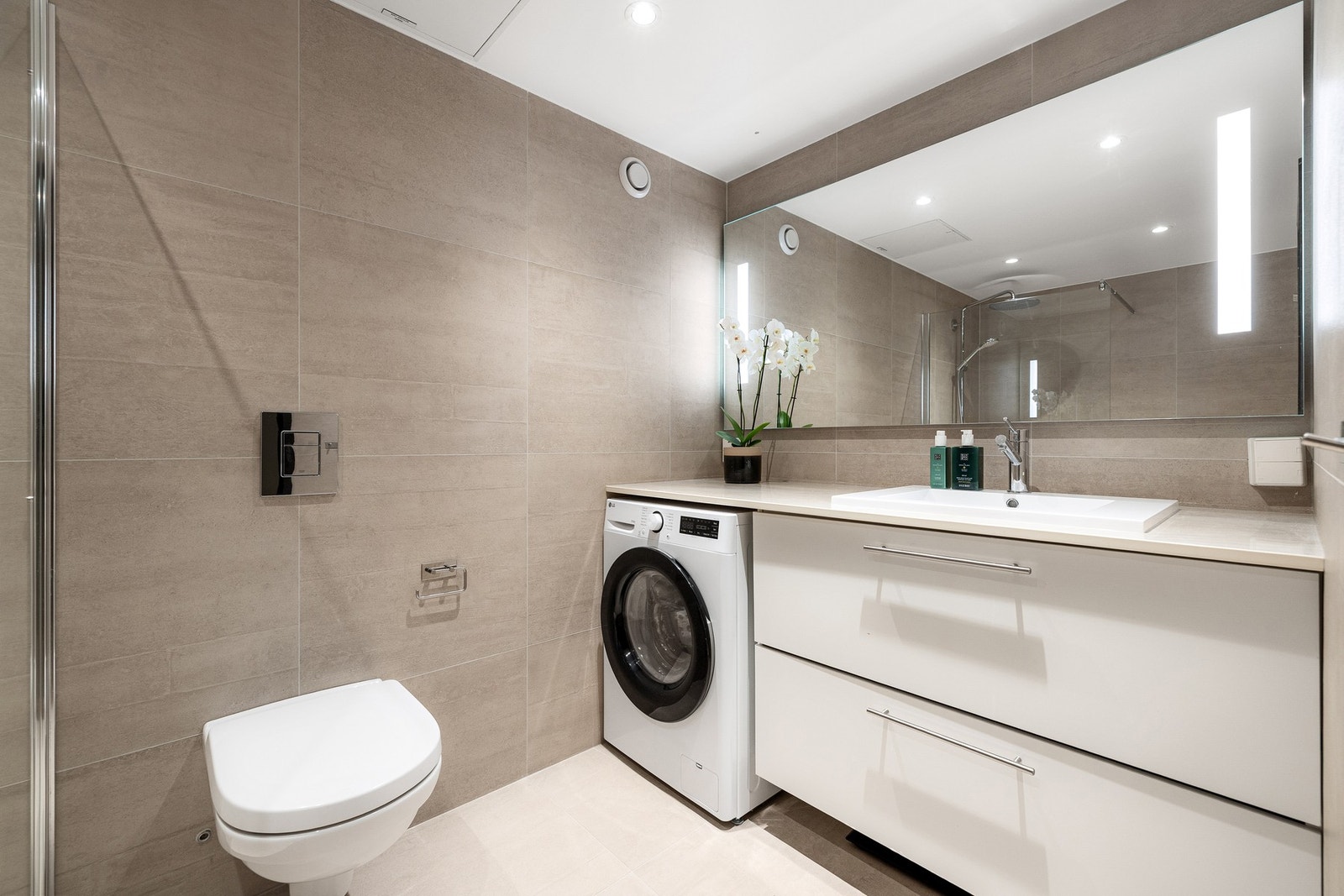 Badet er romslig og har en smart innredning med plass til vaskemaskin under benkeplaten Galleribilde