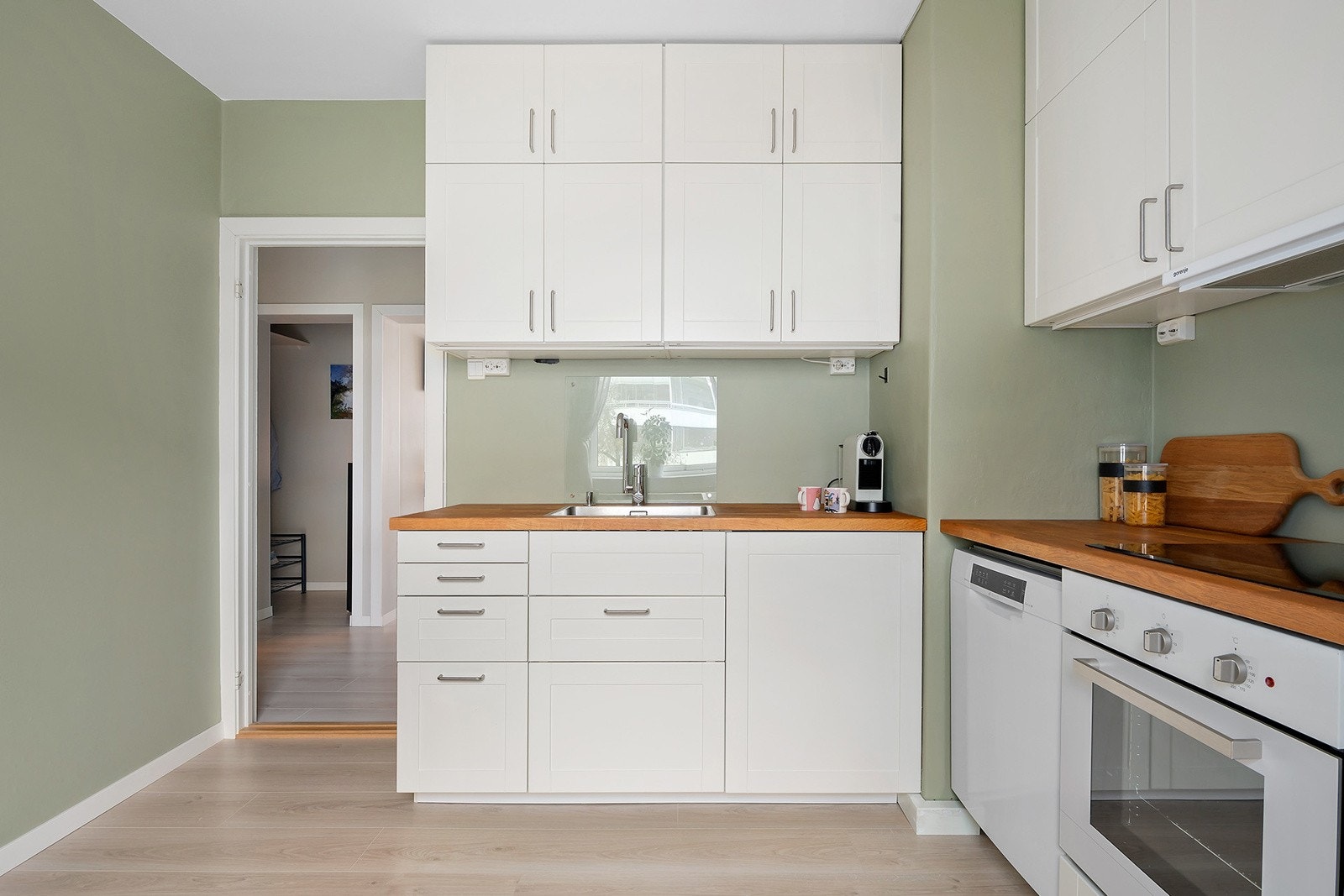 IKEA kjøkkeninnredning med profilerte laminerte skapfronter, finert benkeplate, enkel oppvaskkum, ventilator og innfelte hvitevarer som koketopp, stekeovn, oppvaskmaskin, frittstående kjøl/- fryseskap. Galleribilde