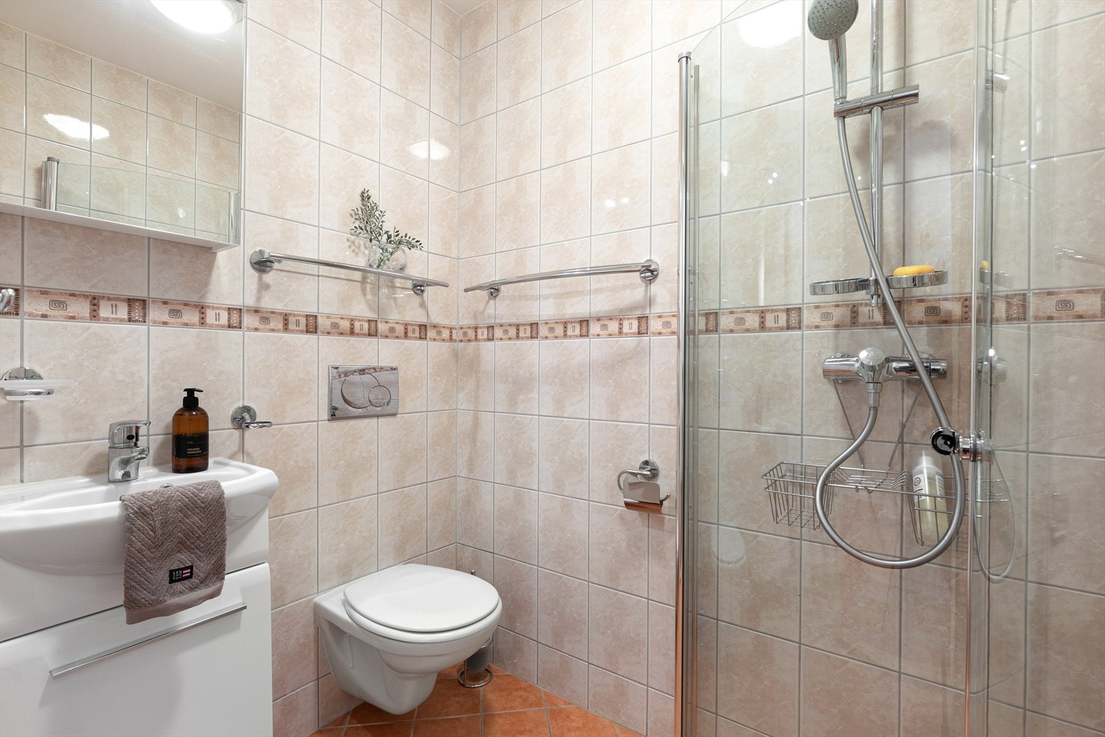 Fliser på golv og veggar, samt kvitmåla gipshimling. Badet er utstyrt med servant, toalett og dusjhjørne. Galleribilde
