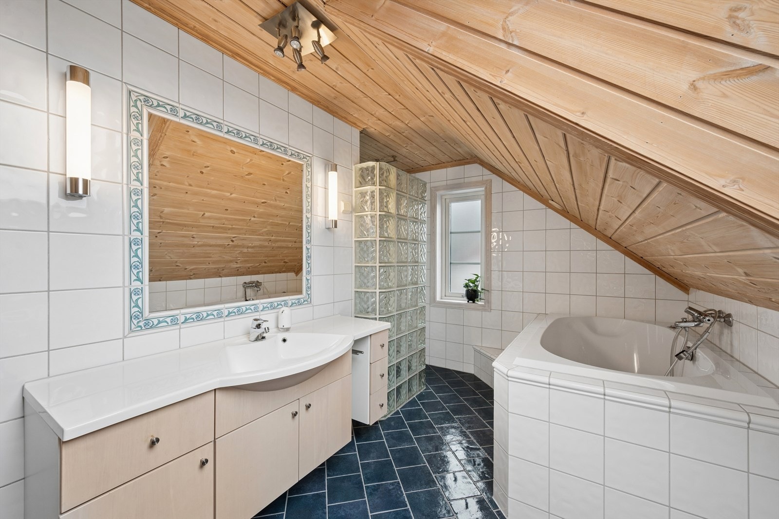 Badet er utstyrt med boblebadekar, gulvstående klosett og en dusjnisje med dusjvegg av glassbyggerstein. Galleribilde