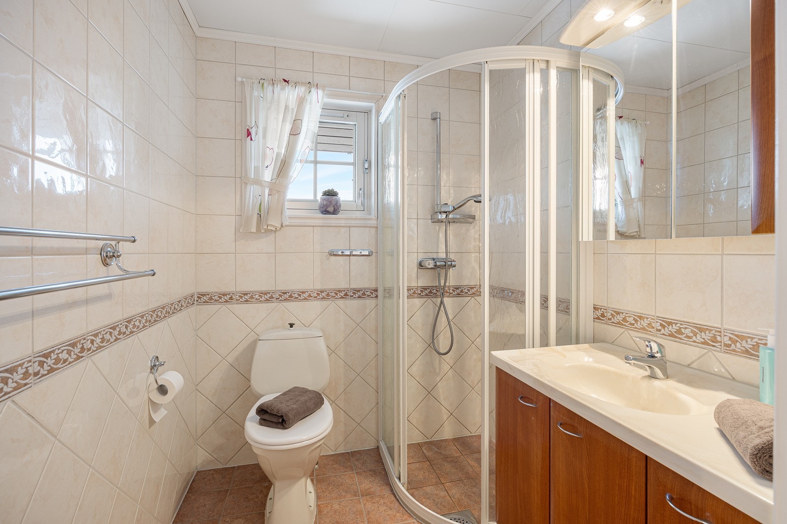 Oppe har badet toalett, gulvvarme og fliser i ulike jordnyanser. Dusjhjørnet er utstyrt med skyvedører Galleribilde