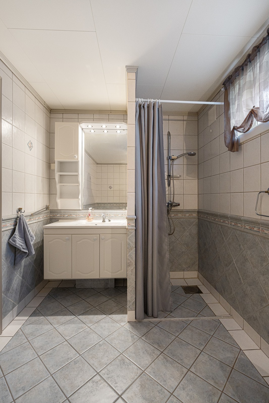 Innredningen består av et hvitt servantskap, et veggskap i samme stil og et speil med belysning over servanten. Galleribilde