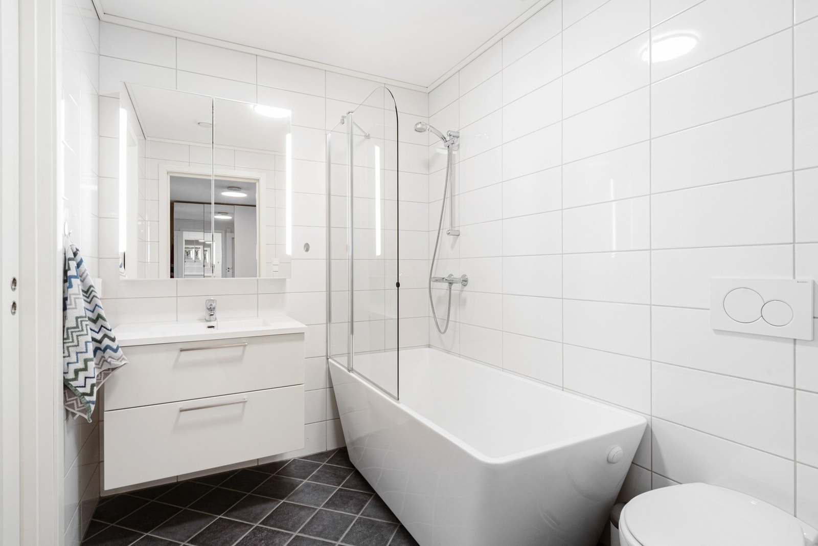 Flott flislagt bad i 1. etasje med gulvvarme, samt baderomsinnredning med heldekkende servant, vegghengt toalett og badekar Galleribilde