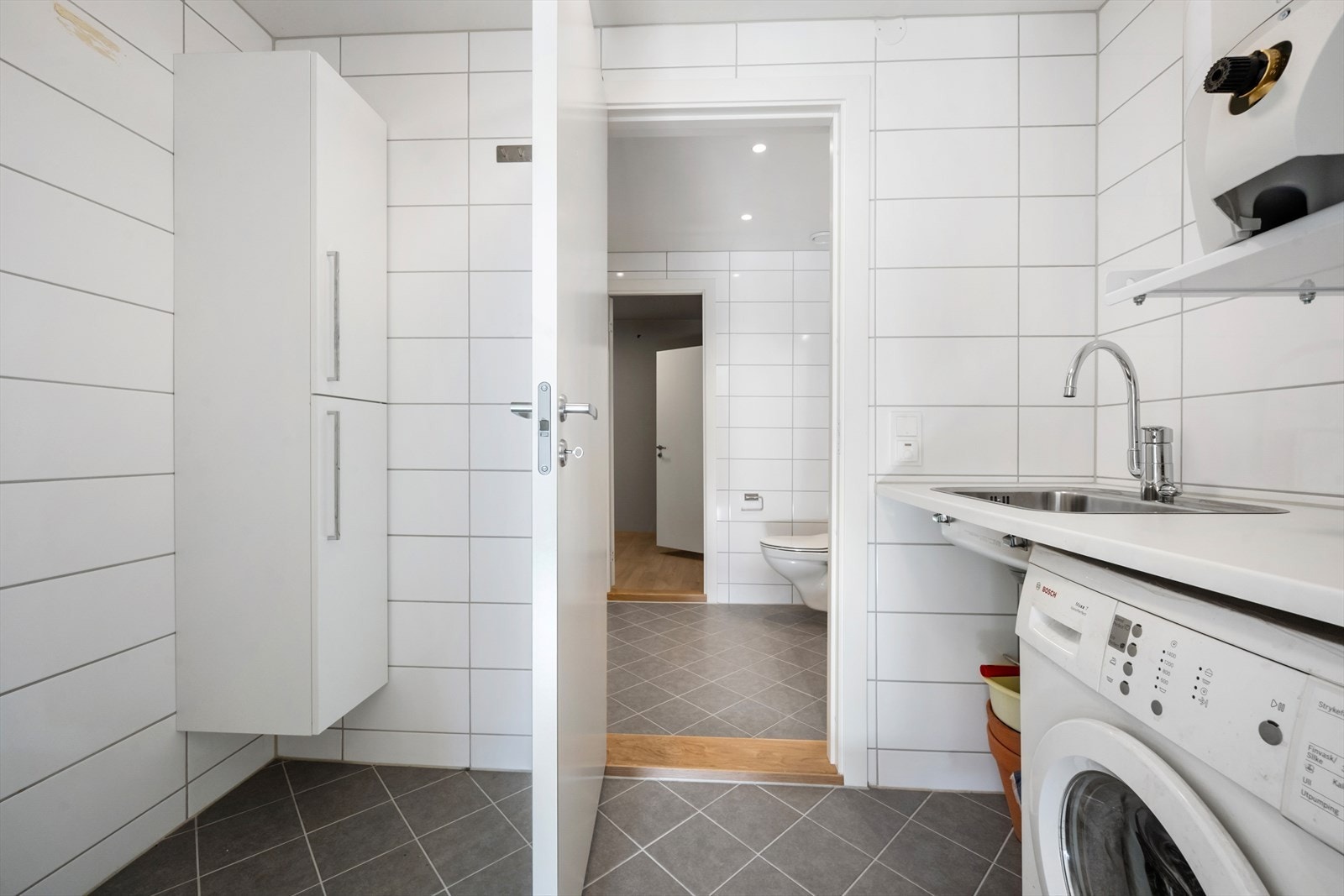 Vaskerommet har flislagt gulv, benkeplate og opplegg for vaskemaskin. Galleribilde