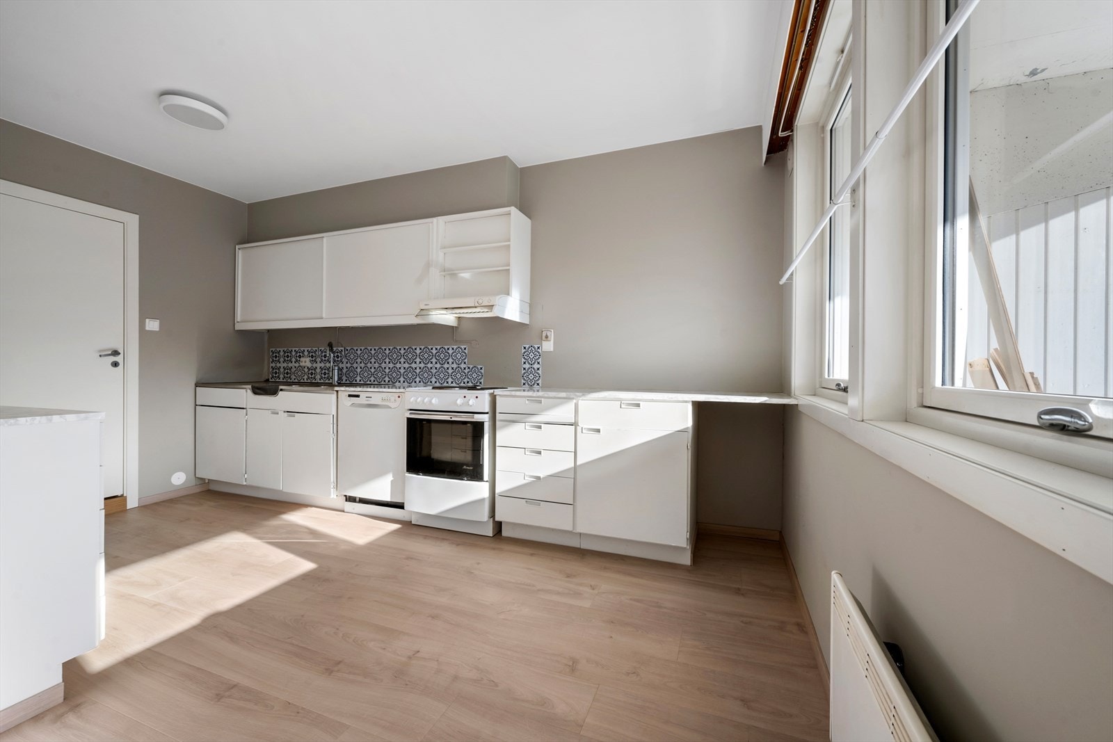 Kjøkkenet har innredning fra byggeåret med malte fronter av finér, laminert benkeplate og stål oppvaskkum. Galleribilde