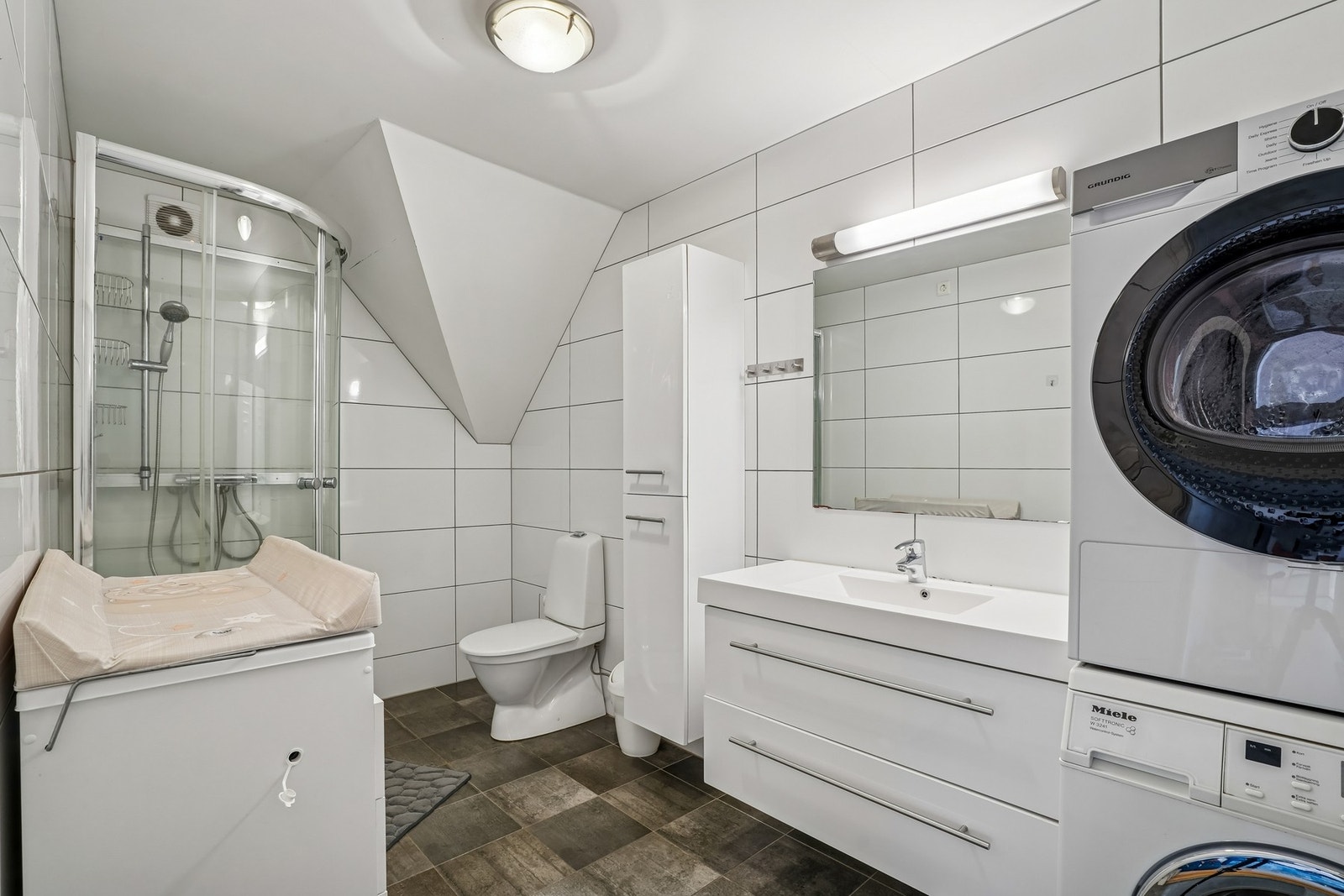 Badet er helfliset med gulvvarme. Innredet med servantinnredning, speil med belysning, dusjkabinett, toalett og opplegg for vaskemaskin. Galleribilde