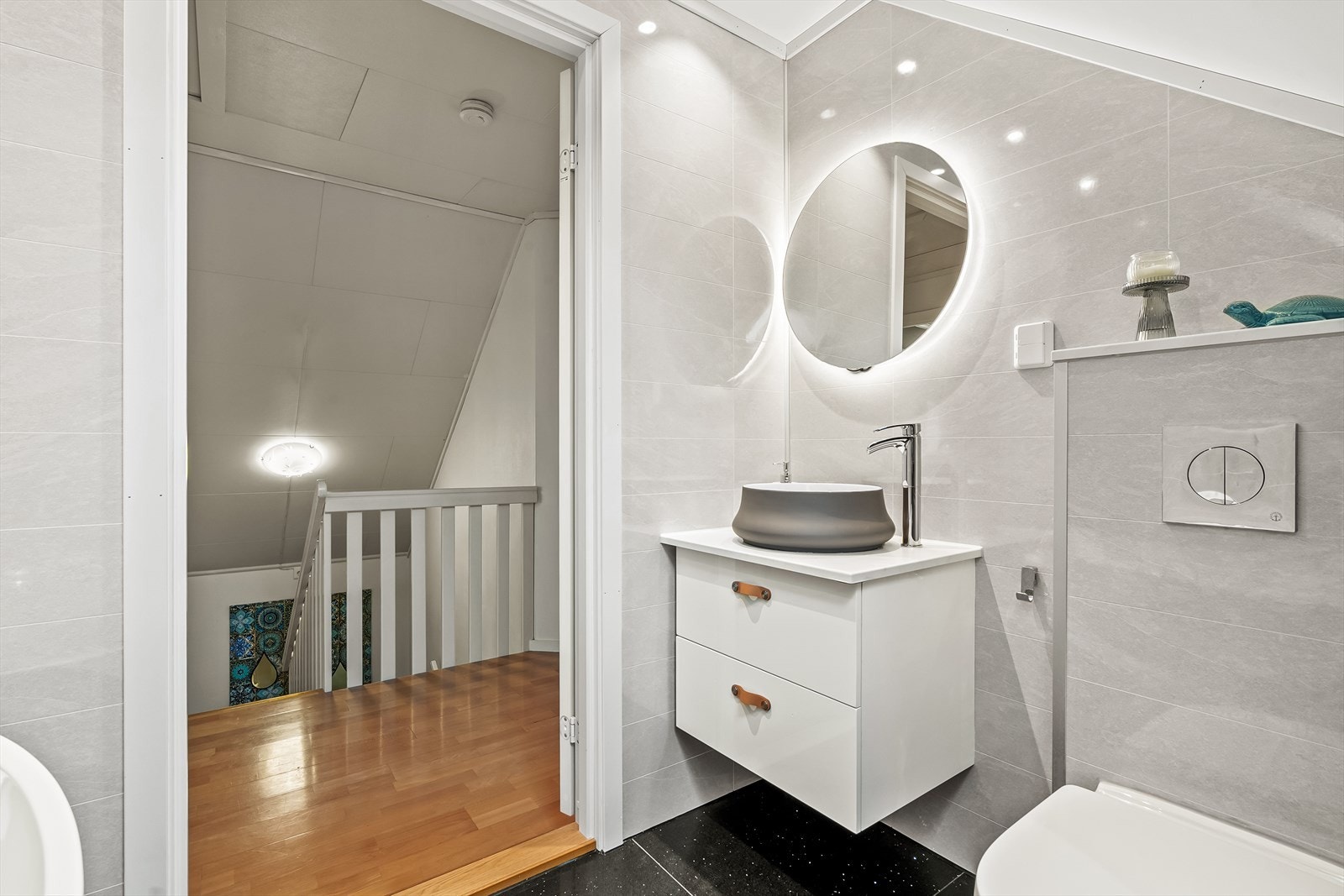 Badet er innredet med baderomsinnredning med glatte folierte fronter, servantbolle på laminat benkeplate, speil montert på vegg over servanten, veggmontert toalett, badekar og dusjutstyr. Galleribilde