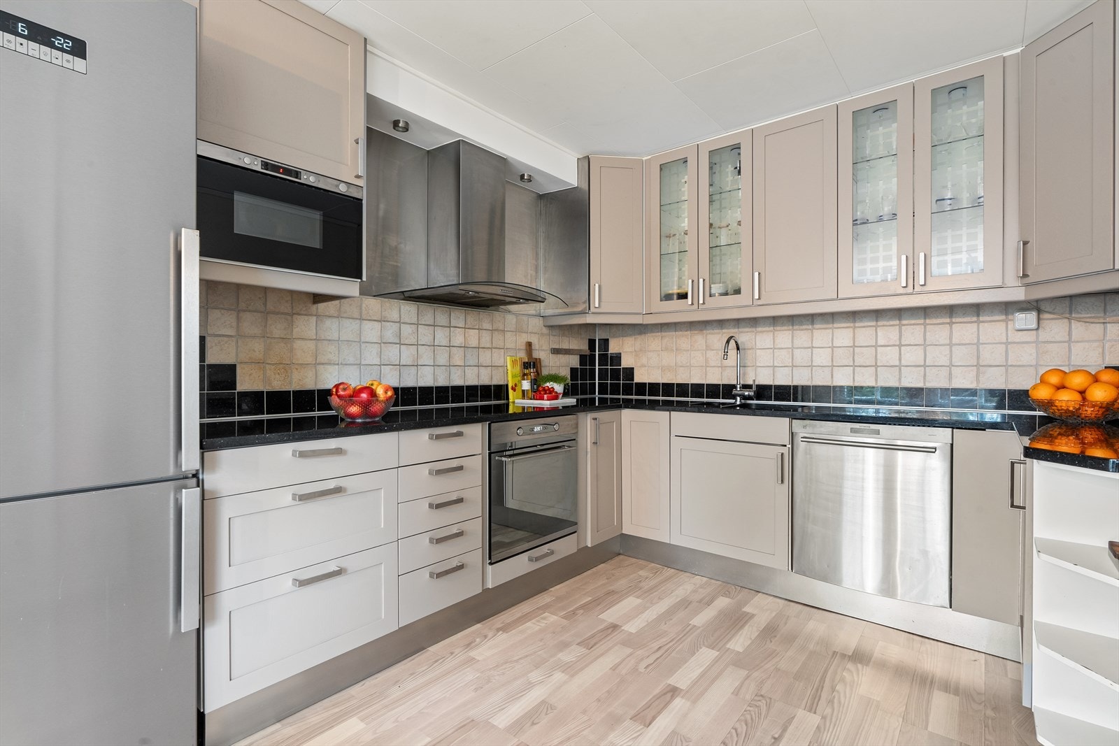 Det er kvartsitt (stein) benkeplate med underlimt kum i rustfritt stål, fliser på vegg over benkeplaten og lys under overskap. Galleribilde