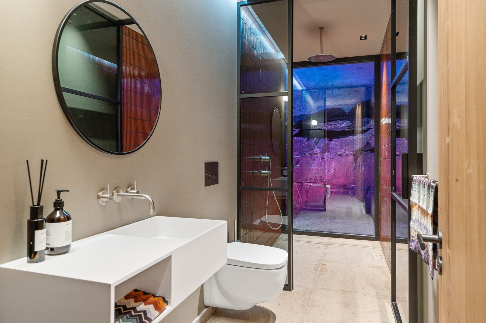 Fantastisk detalj hvor man ser opplyst råfjell bak glassveggen på badet. Galleribilde