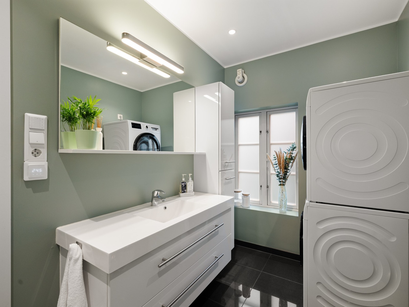 Badet har et stilrent uttrykk der store, mørke gulvfliser kombineres med hvite veggfliser og plater malt med en mintgrønn våtromsmaling i 2021. Galleribilde