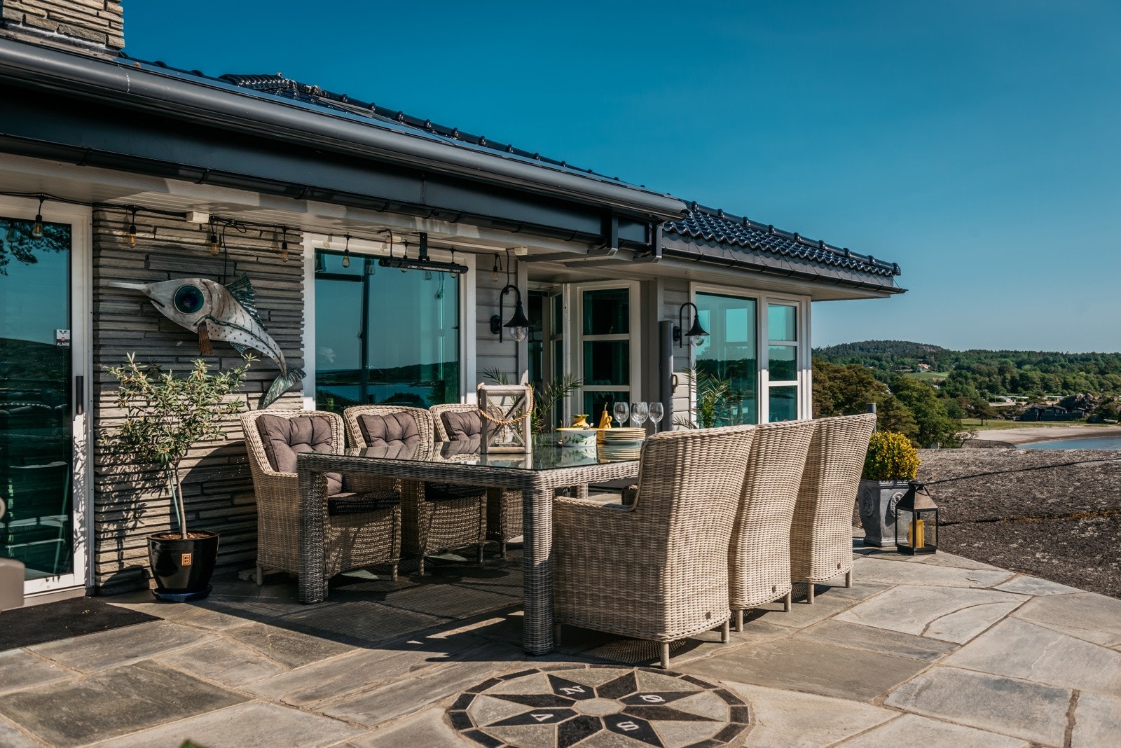 Hytta har en stor og åpen uteplass med steinbelagt dekke og nydelig utsikt mot sjøen - et perfekt samlingspunkt for familie og gjester Galleribilde