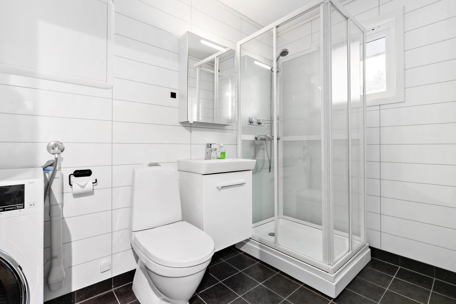 Bad/vaskerom har flislagt gulv med varmekabler. Her er det innredet med dusjkabinett, servant med underskap,
toalett og opplegg for vaskemaskin. Galleribilde