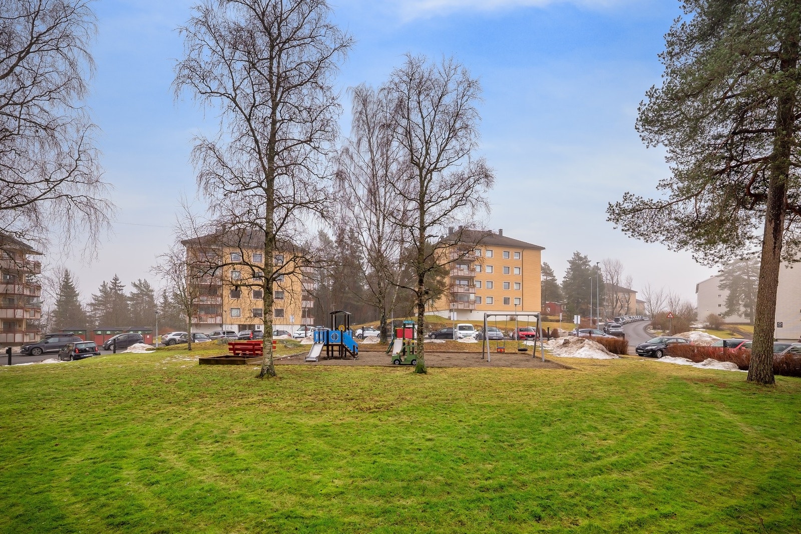 Hyggelig uteområde med gressplen, trær og lekeplasser Galleribilde
